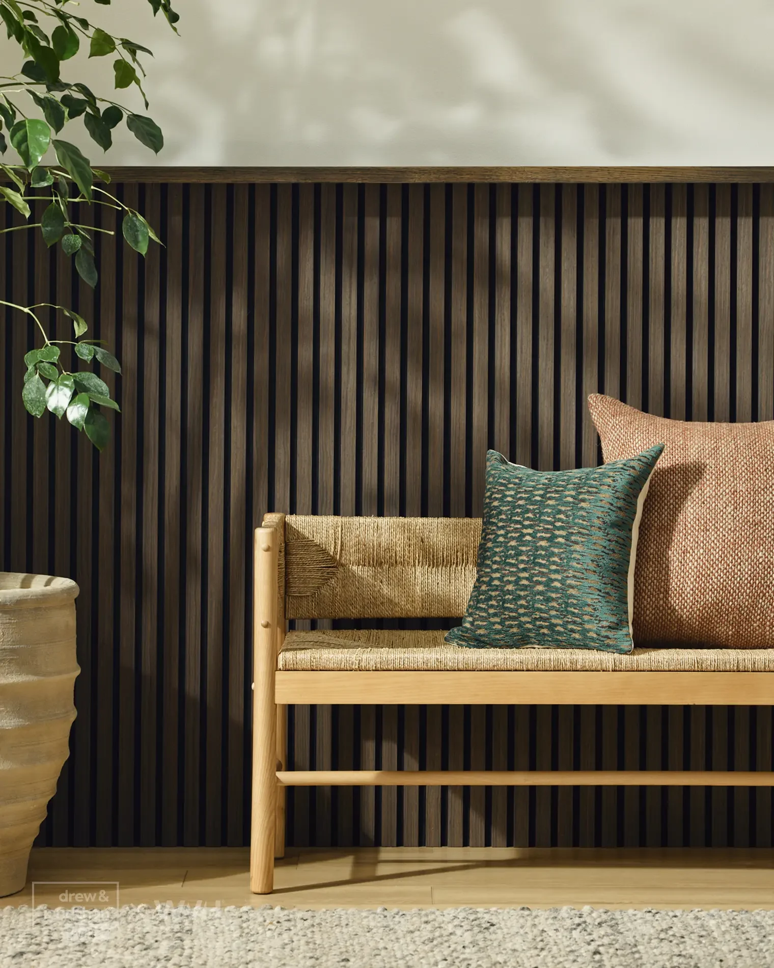 Interior with a wooden bench and decorative pillows, potted plant on a textured carpet, black slatted wall