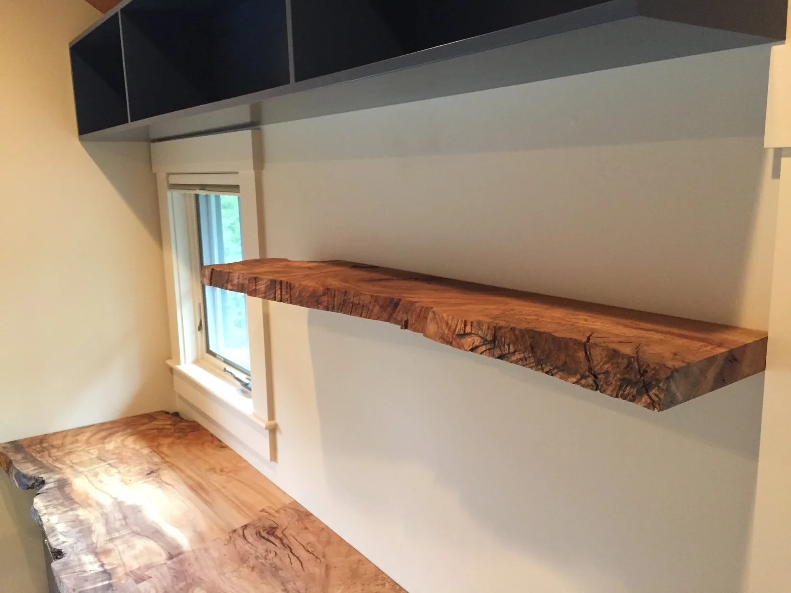 Wooden shelves mounted on a white wall near a window in a room.