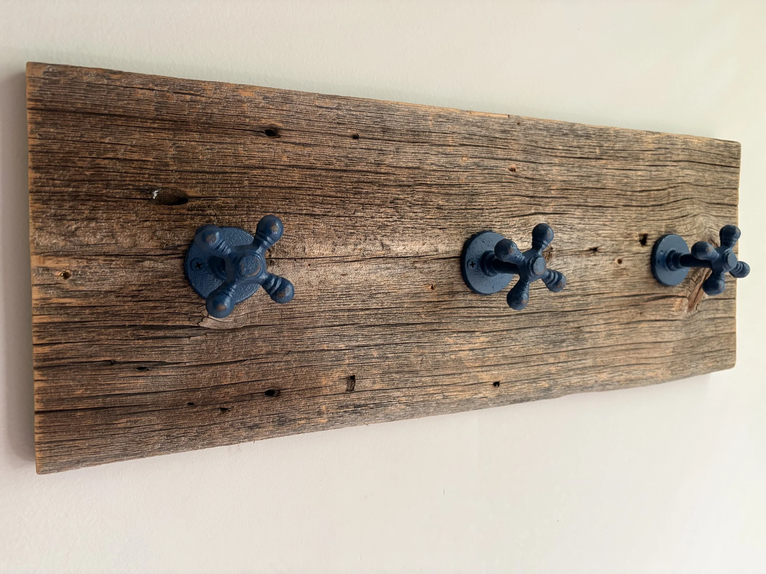 A wooden wall-mounted coat rack with three blue metal hooks attached to a piece of weathered wood.