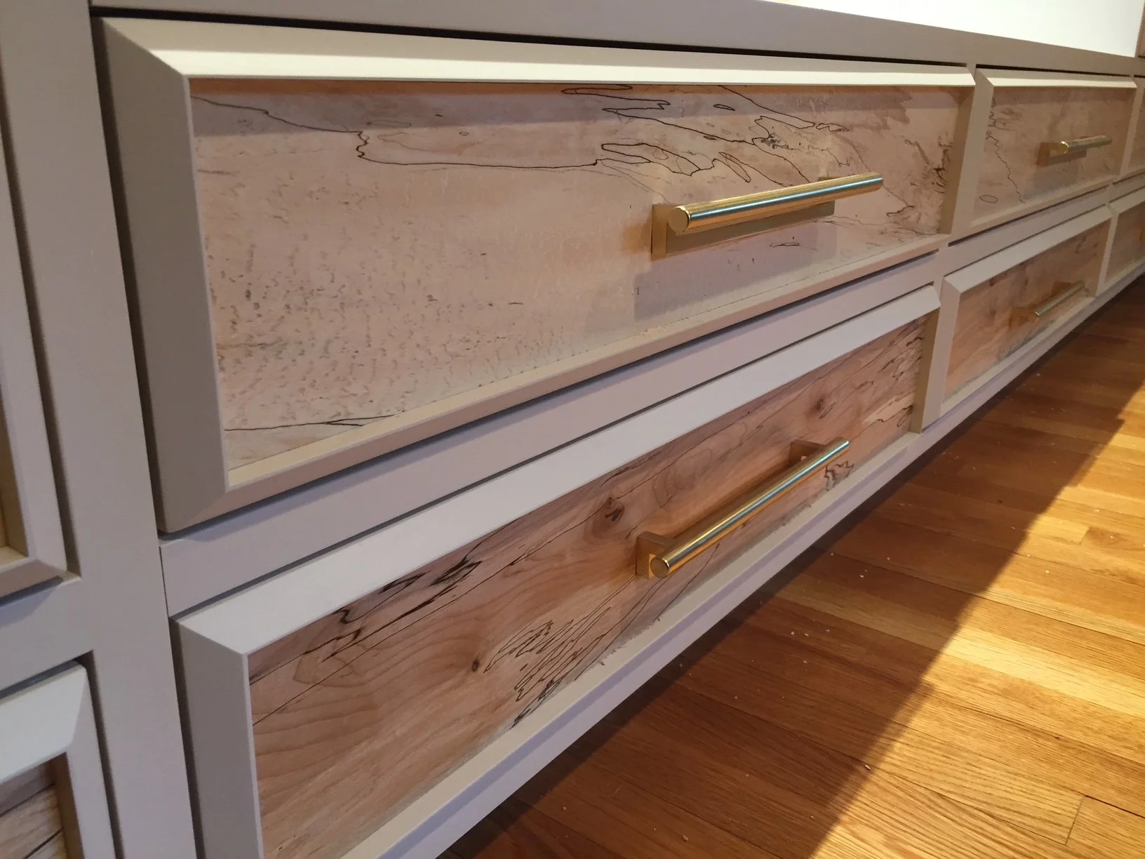 Close-up of a modern dresser with a combination of white and natural wood finished drawers, featuring sleek gold handles, on a wooden floor.