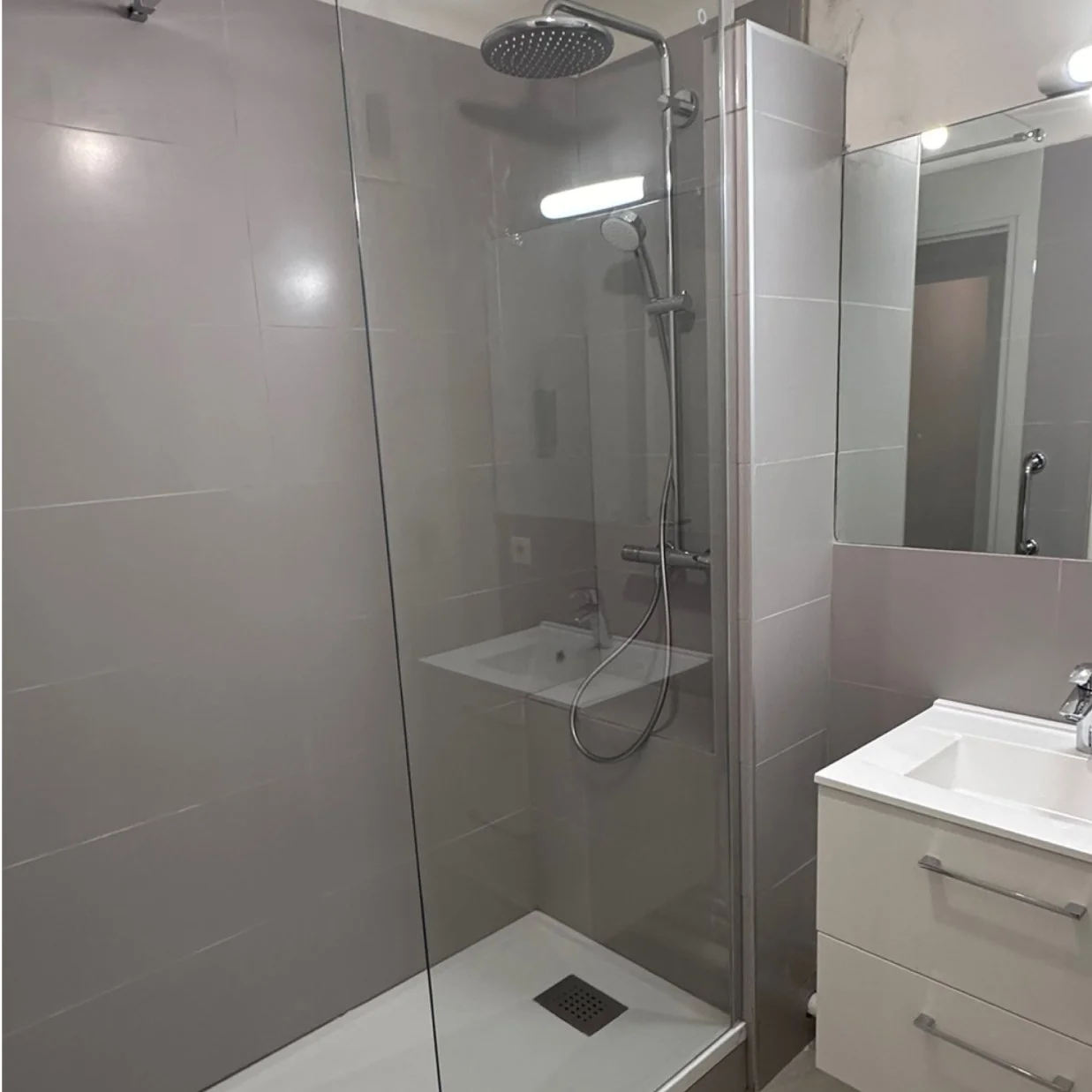 Salle de bain avec douche, lavabo et miroir.
