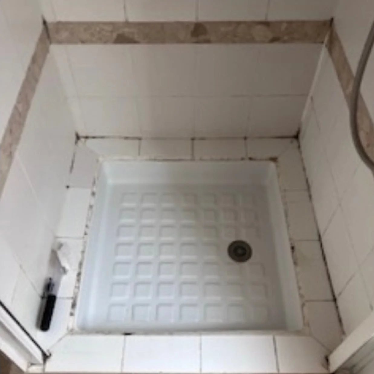 Douche avec un bac en plastique, inutilement sortant de la zone de carrelage, avec des tuiles murales blanches, en cours de rénovation.