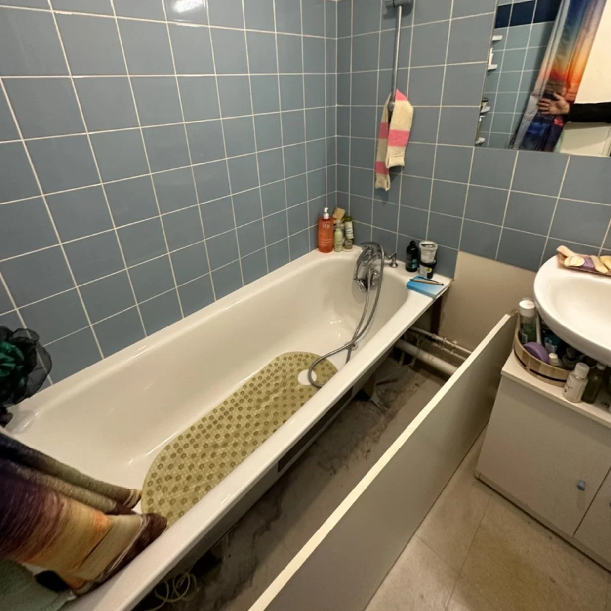 Baignoire dans une salle de bain avec des murs en carreaux bleus, un miroir, un évier avec des accessoires et des produits de toilette