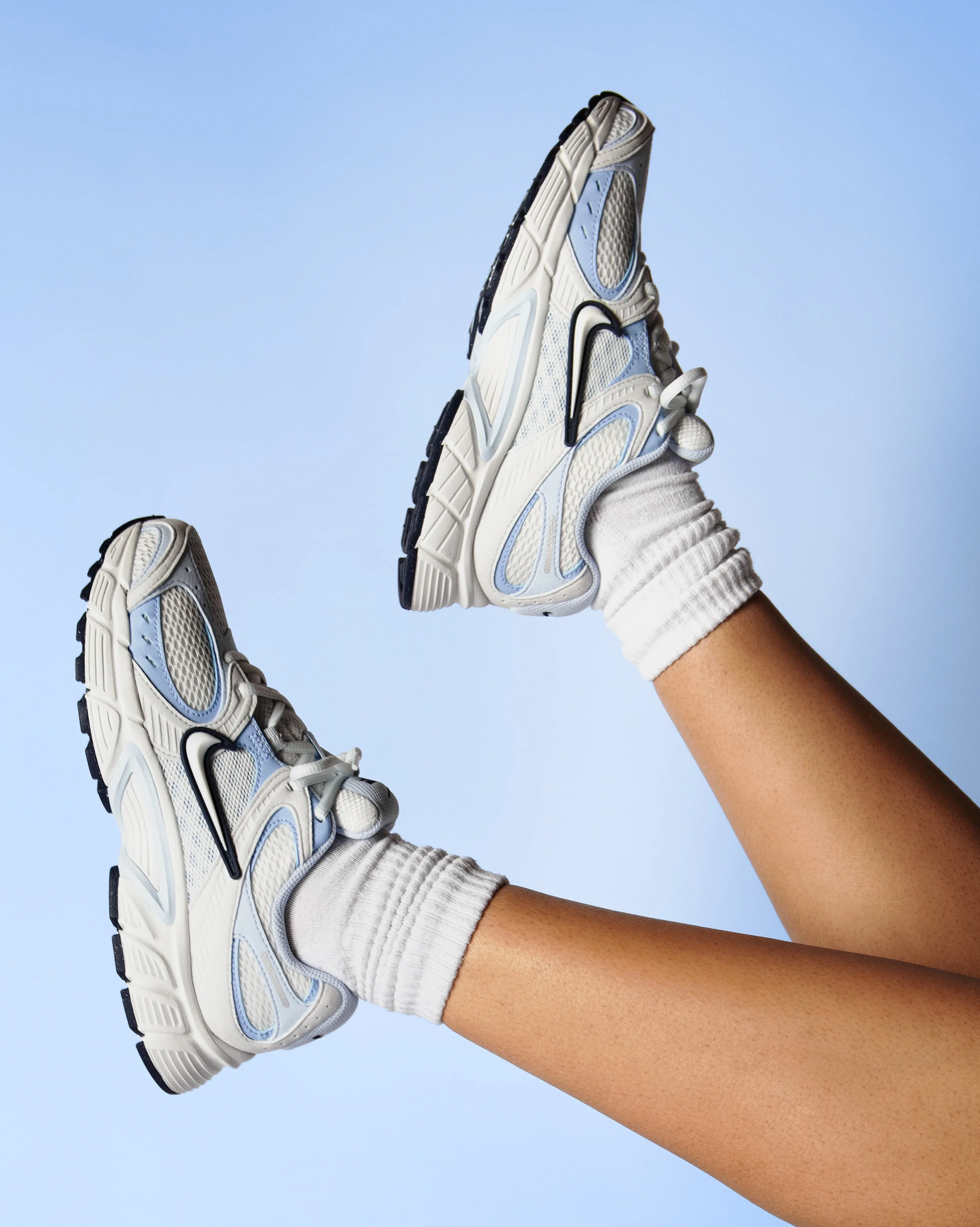 Feet lifted in the air wearing a white and blue athletic shoe, elevated against a light blue background.