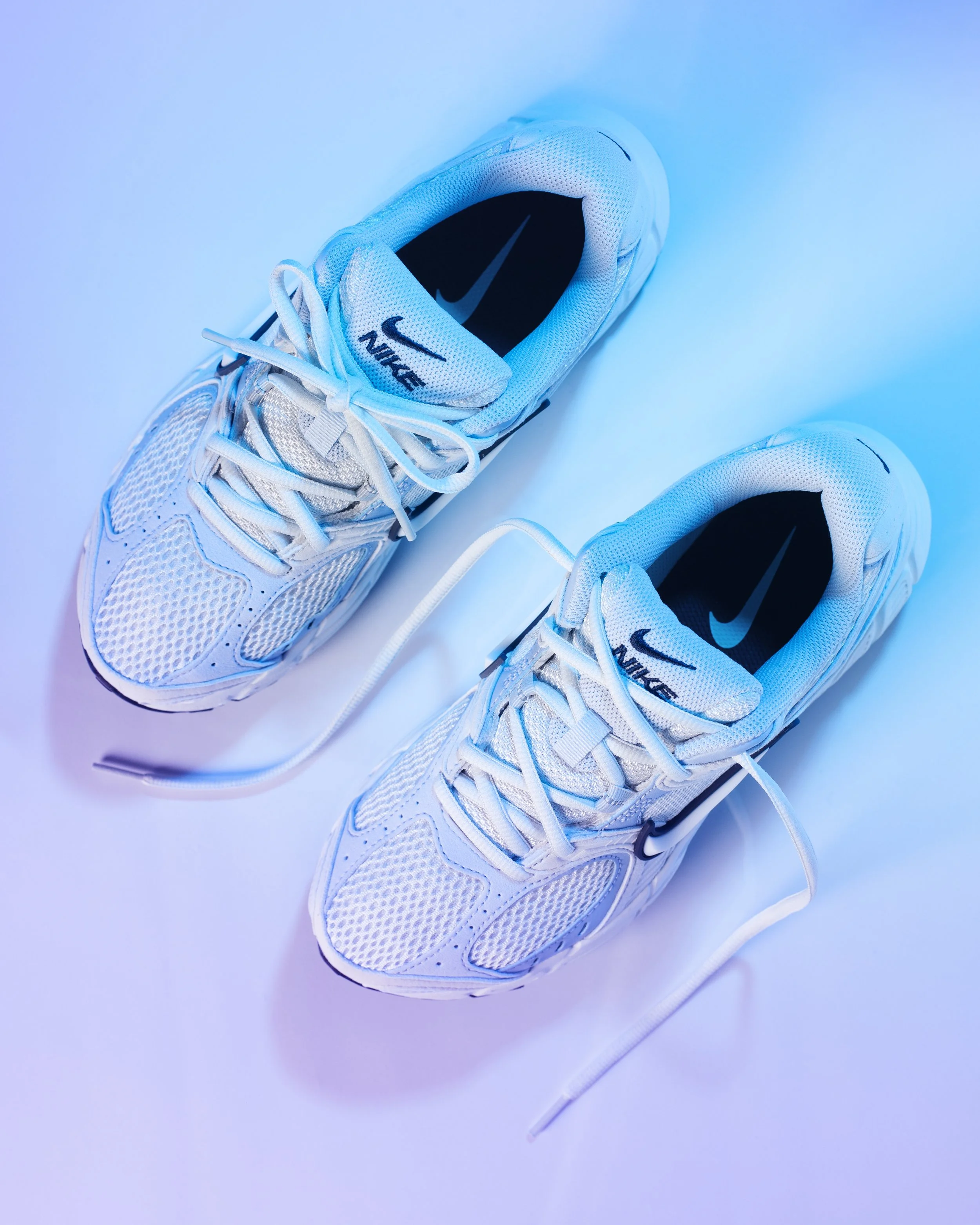 Pair of white Nike running shoes on a white surface with white laces.