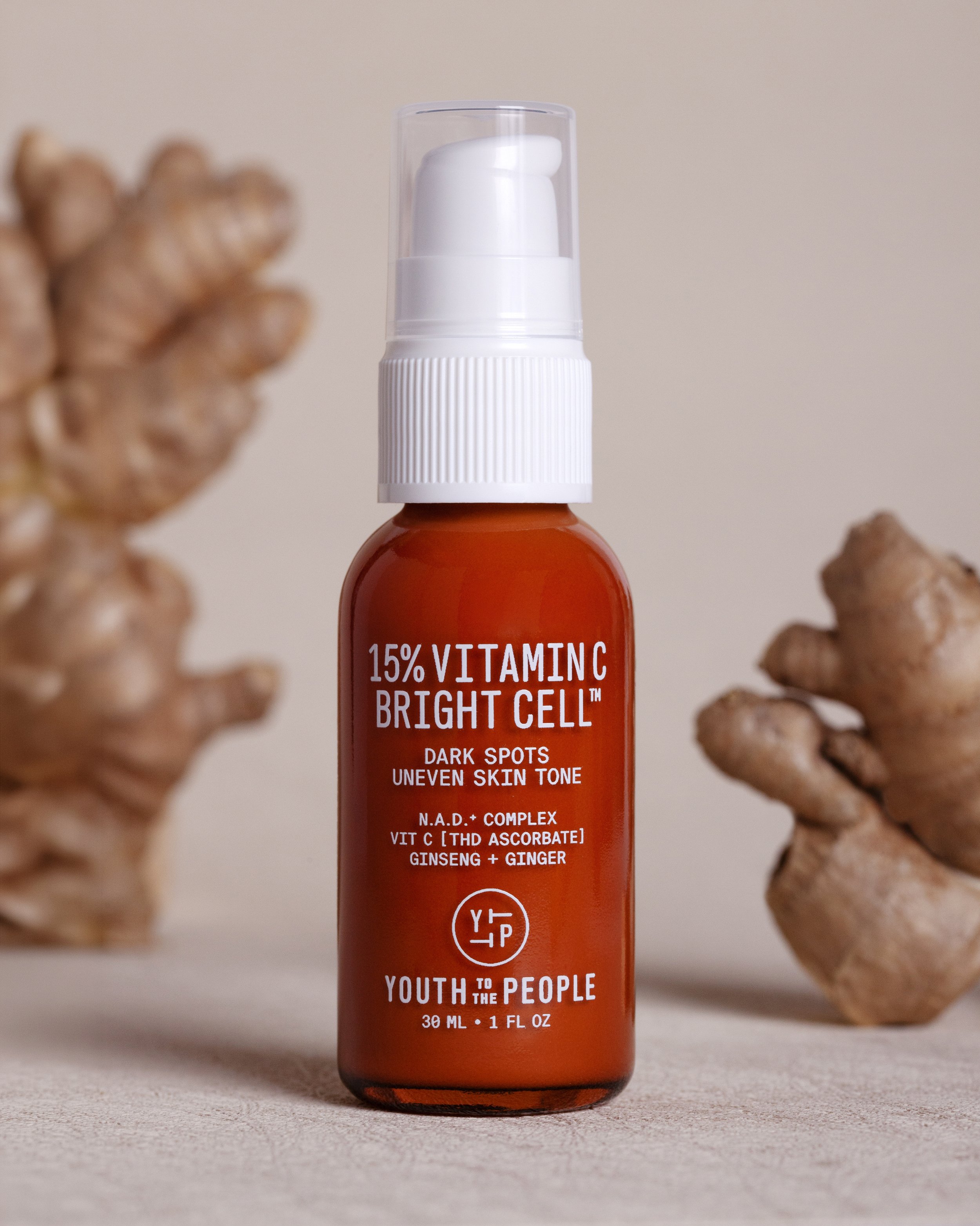 Bottle of Vitamin C brightening skincare serum with ginger, ginseng, and other ingredients, surrounded by ginger roots.