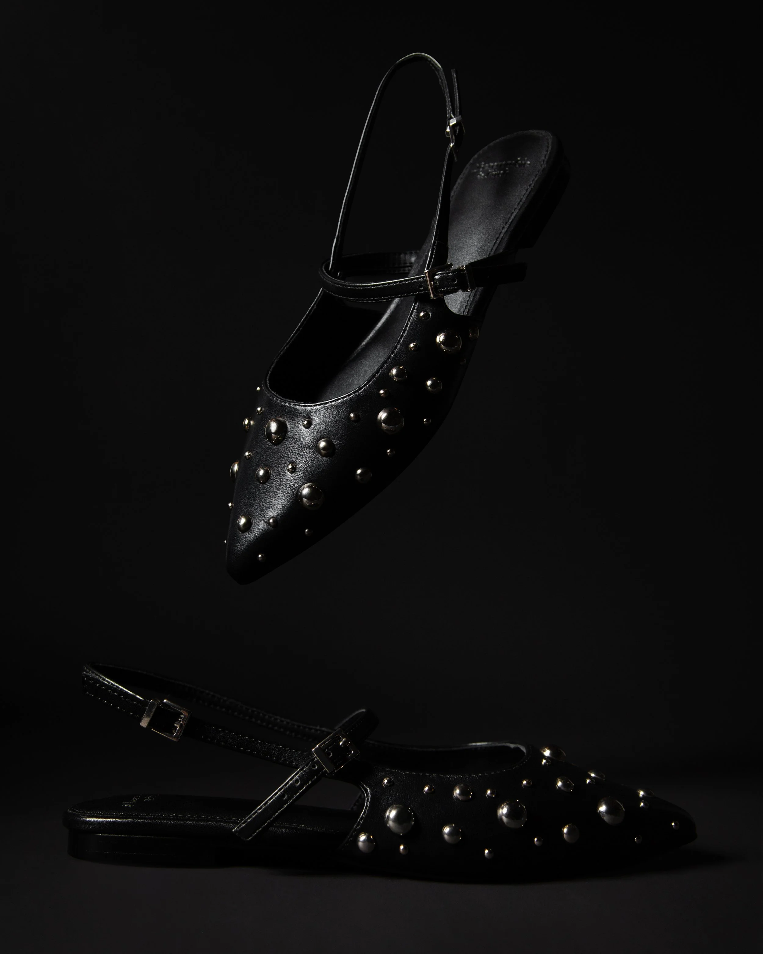 Black stuffed flats, hanging on a black background.