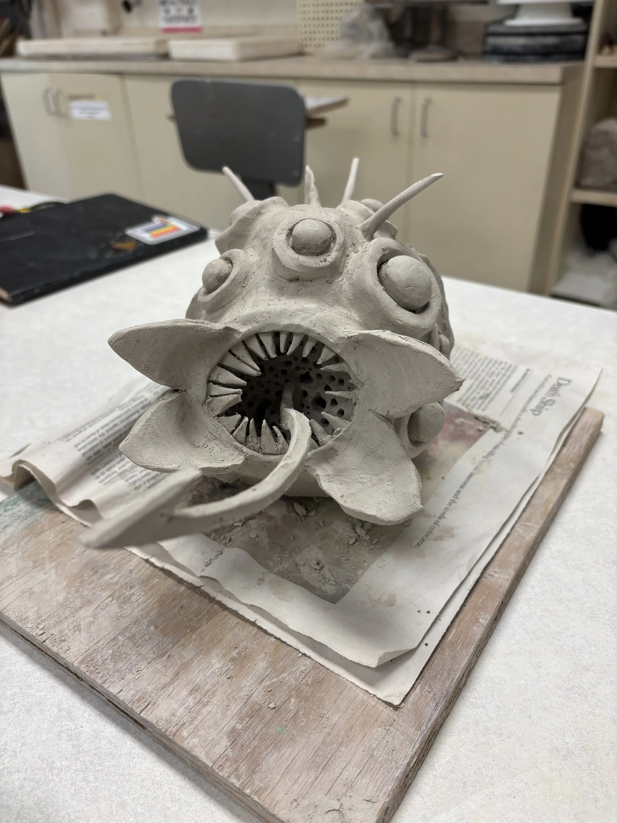 Unfired greenware ceramic sculpture of a fantastical spiky creature with large eyes and an open toothed mouth, made by a PVCC student in Malenka Luckett's ceramics class
