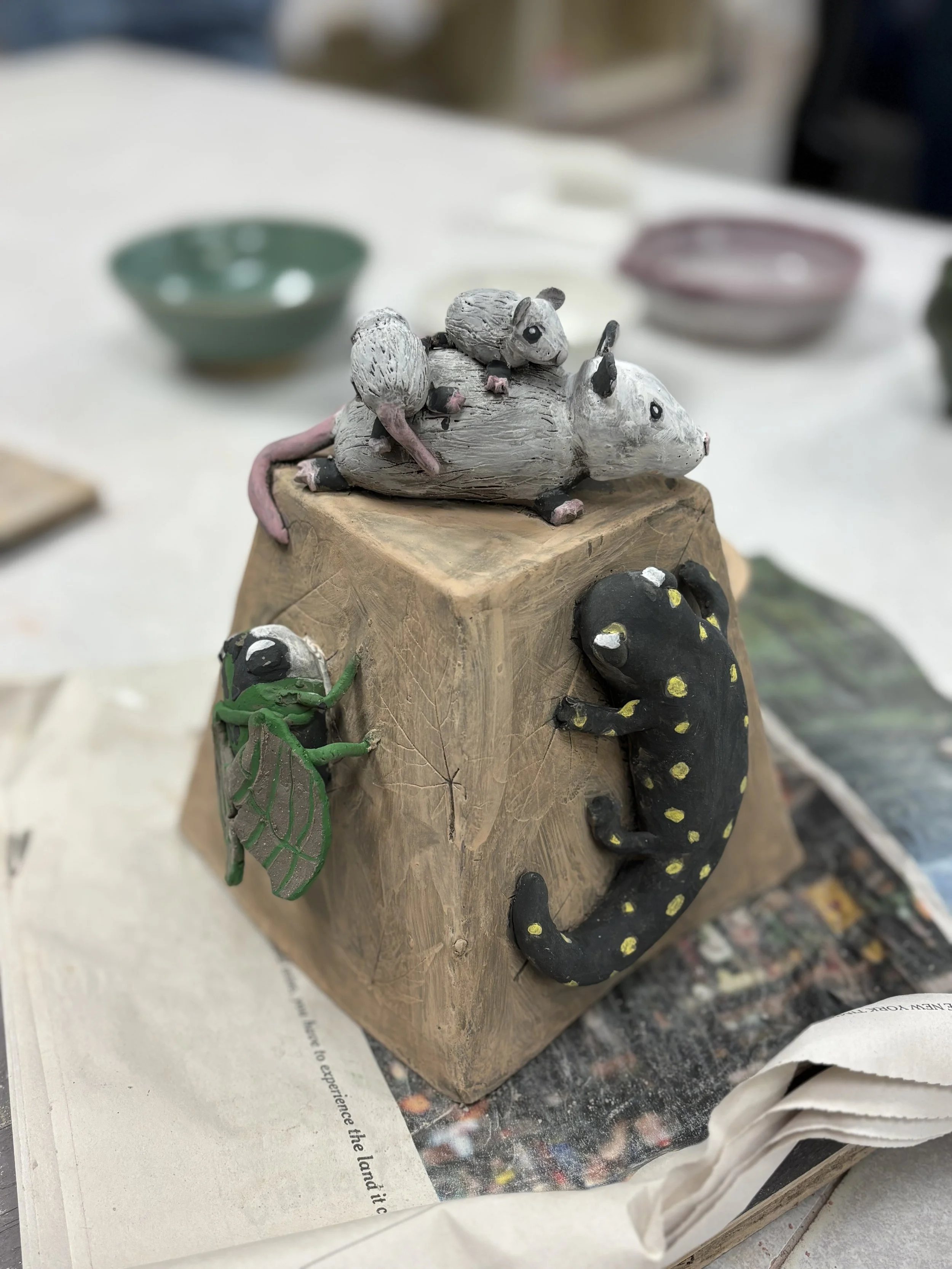 Handbuilt ceramic sculpture by a PVCC student featuring three possums, a spotted salamander, and a cicada climbing a clay block, made in Malenka Luckett's ceramics class at Piedmont Virginia Community College