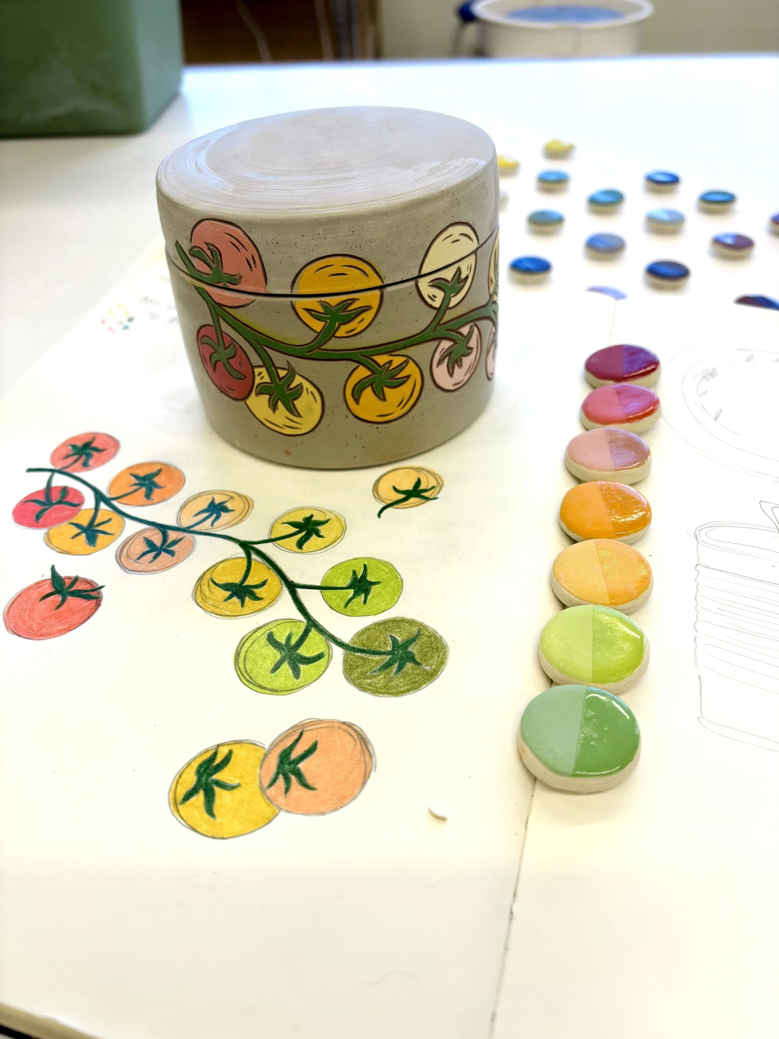 Handmade ceramic jar in progress with hand-painted cherry tomato vine illustration, shown alongside a color sketch and row of underglaze test tiles in warm tones