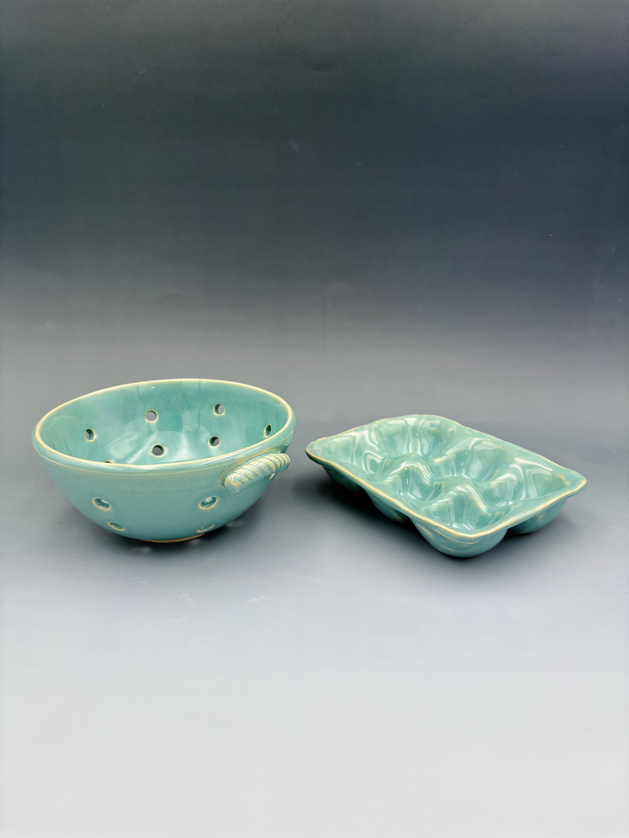 Handmade ceramic berry bowl with pierced drainage holes and a six-cup egg tray, both in matching teal glaze, by student Reese McCardle made in Malenka Luckett's ceramics class"

Image 3 — Green mug:
"Handmade wheel-thrown ceramic mug in sage green gl