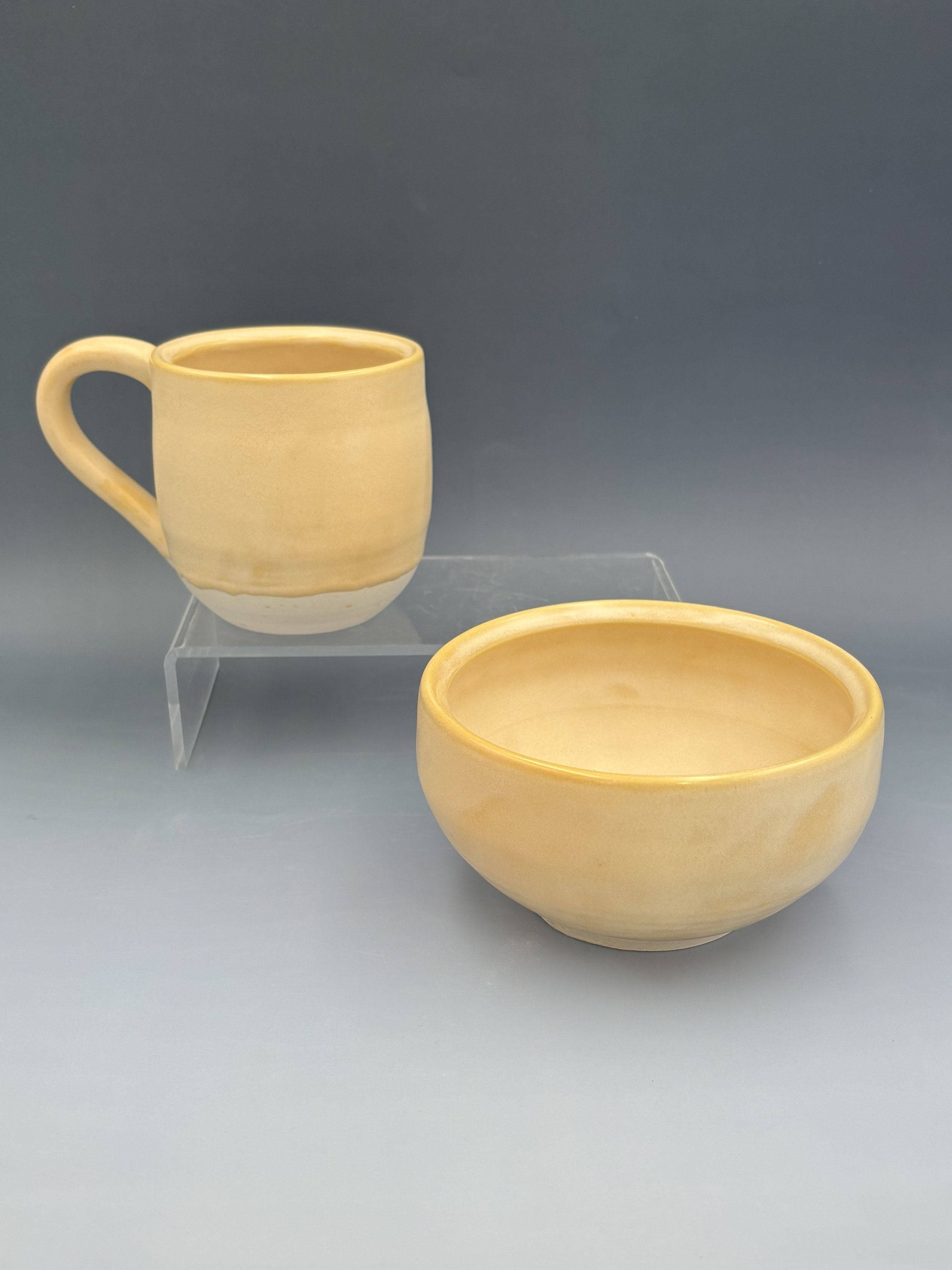 Handmade wheel-thrown ceramic mug and bowl by student Lisa Bowers in warm golden yellow glaze with unglazed white foot, made in Malenka Luckett's ceramics class