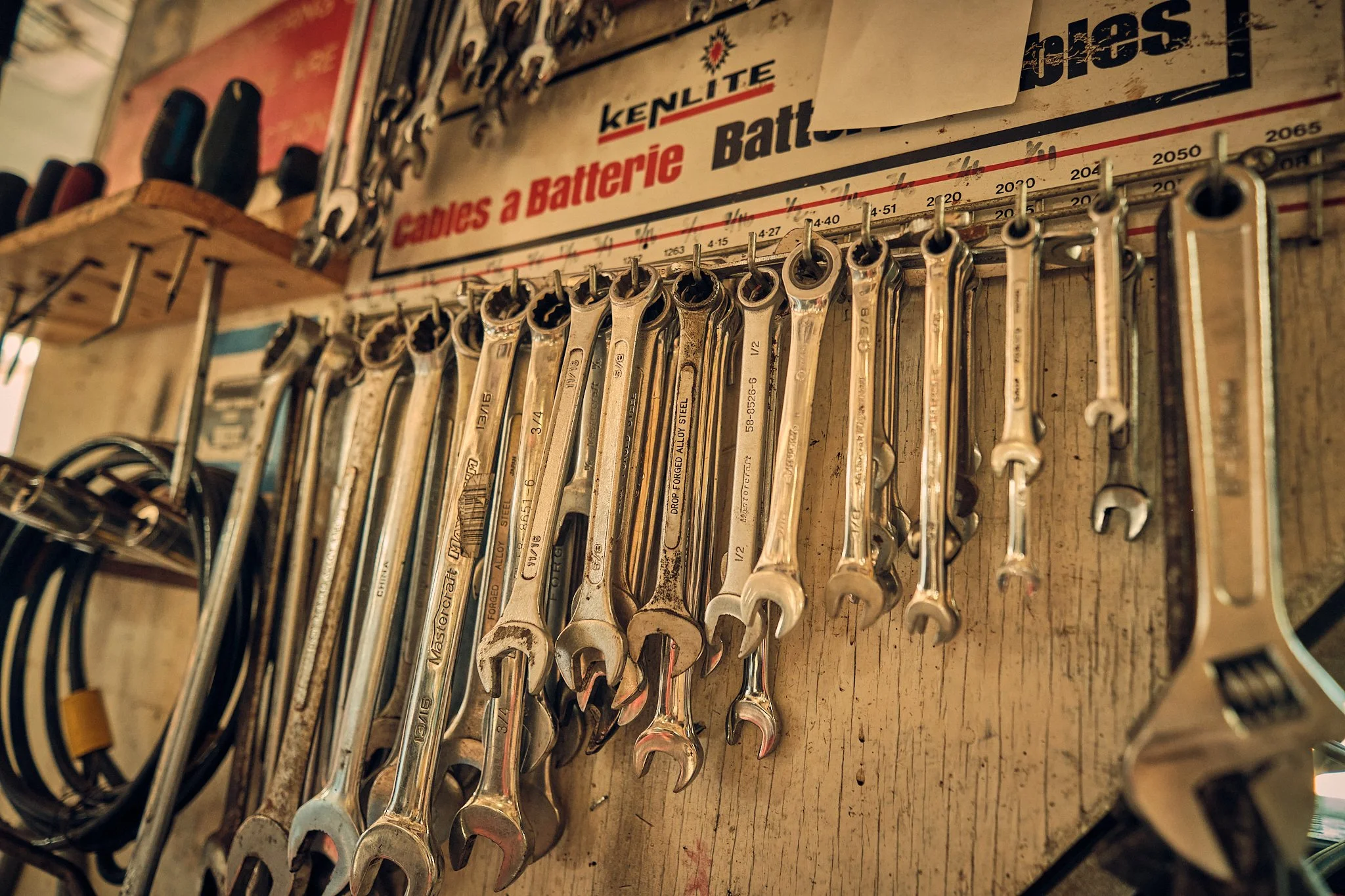 A collection of wrenches hanging on a wooden board with a sign above them indicating they belong to a battery charger or tools for battery care.