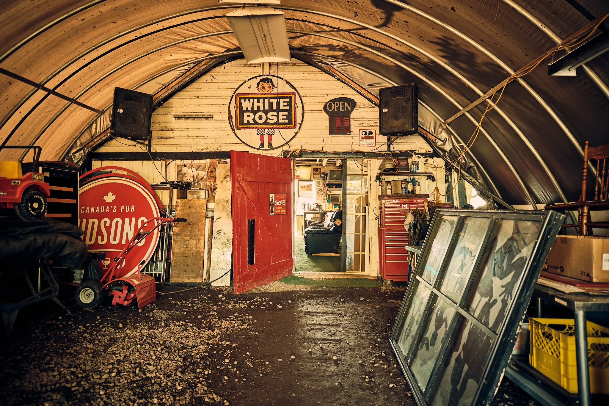 Interior of a rustic store or garage with various items including framed pictures, tools, and large framed glass panes leaning against the wall.