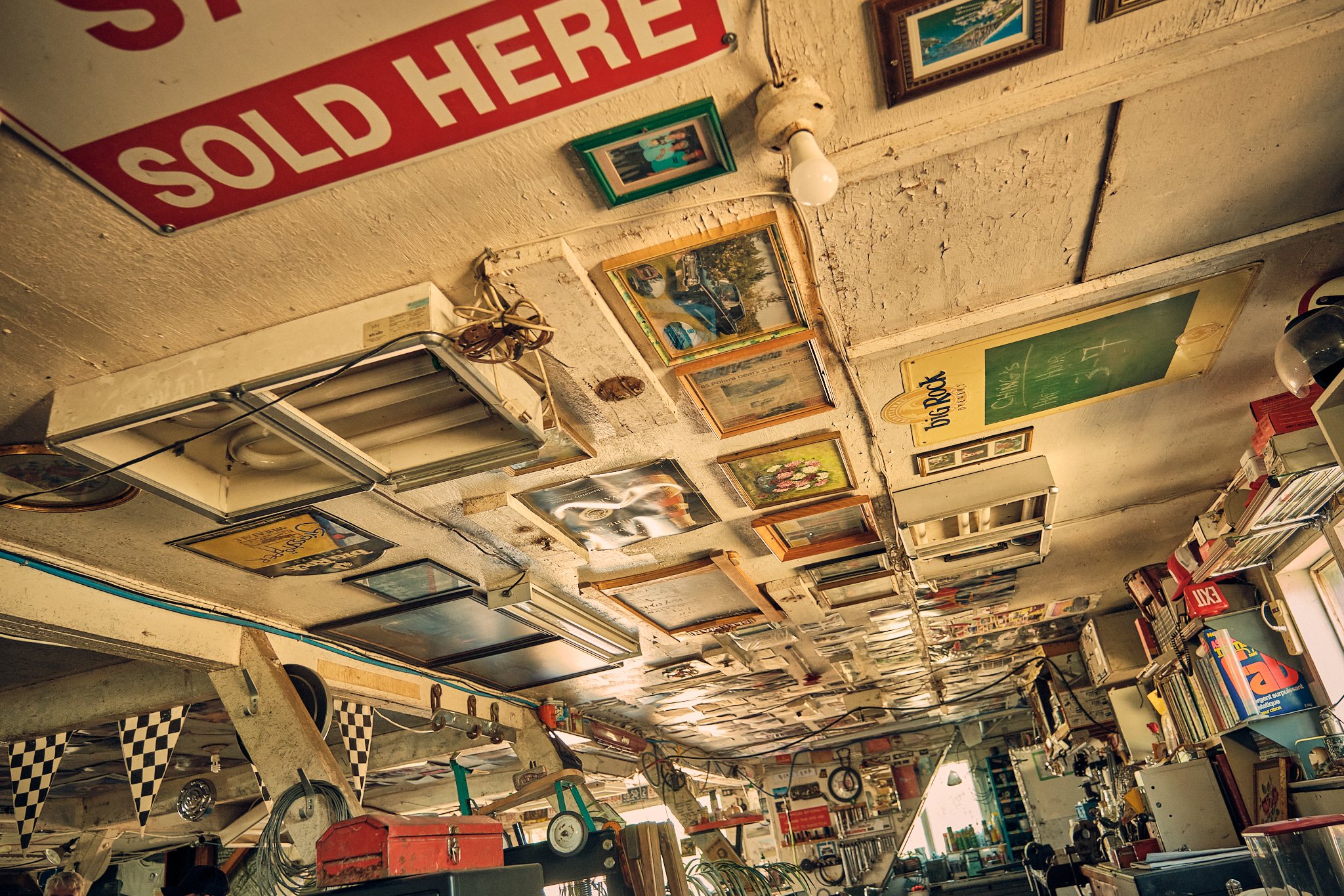Interior of a vintage store or shop with various framed pictures, signs, and objects on the wall, and shelves filled with books and items.