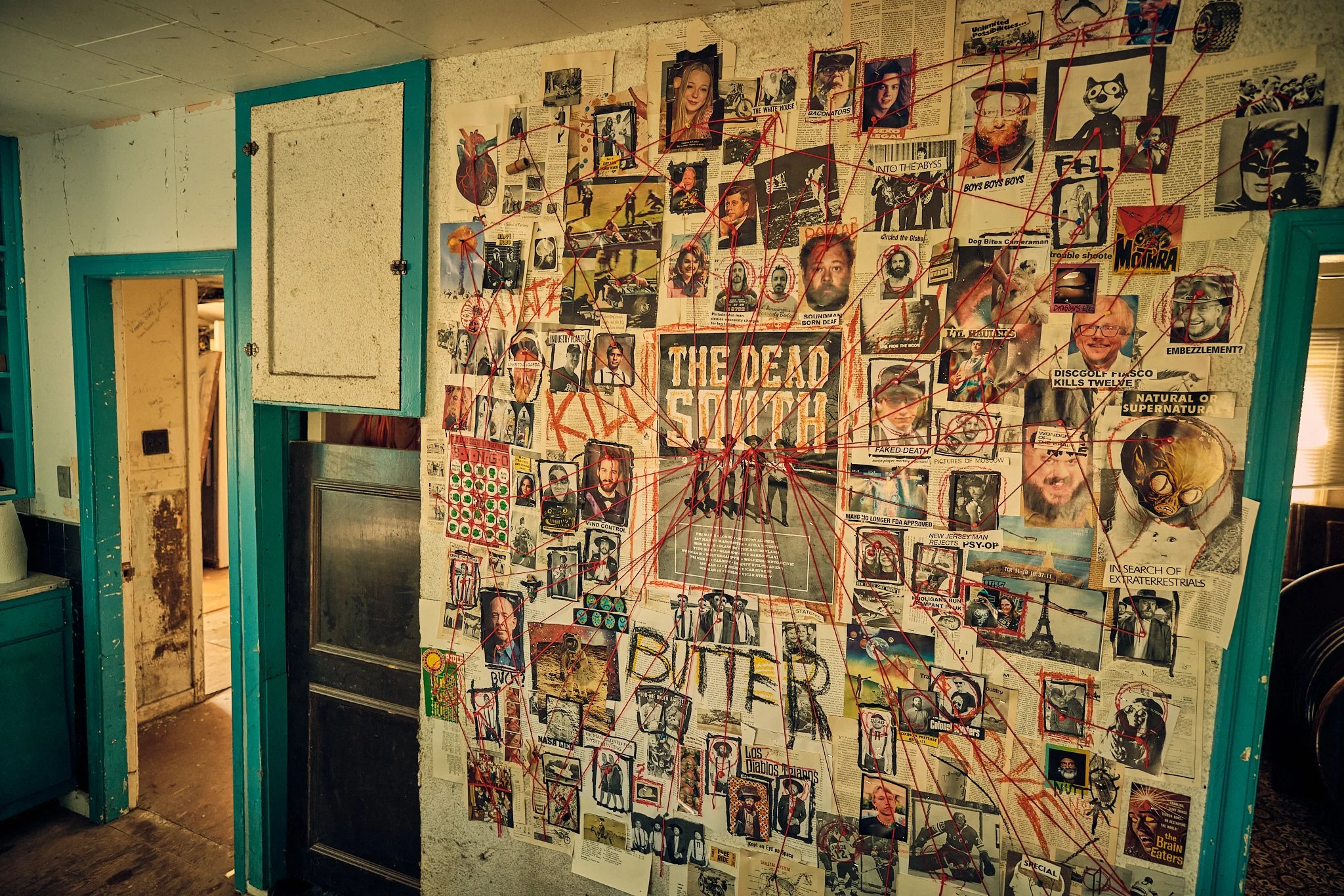 A wall covered with newspaper clippings, photographs, and red string connecting different images, with a large sign reading "THE DEAD SOULS".