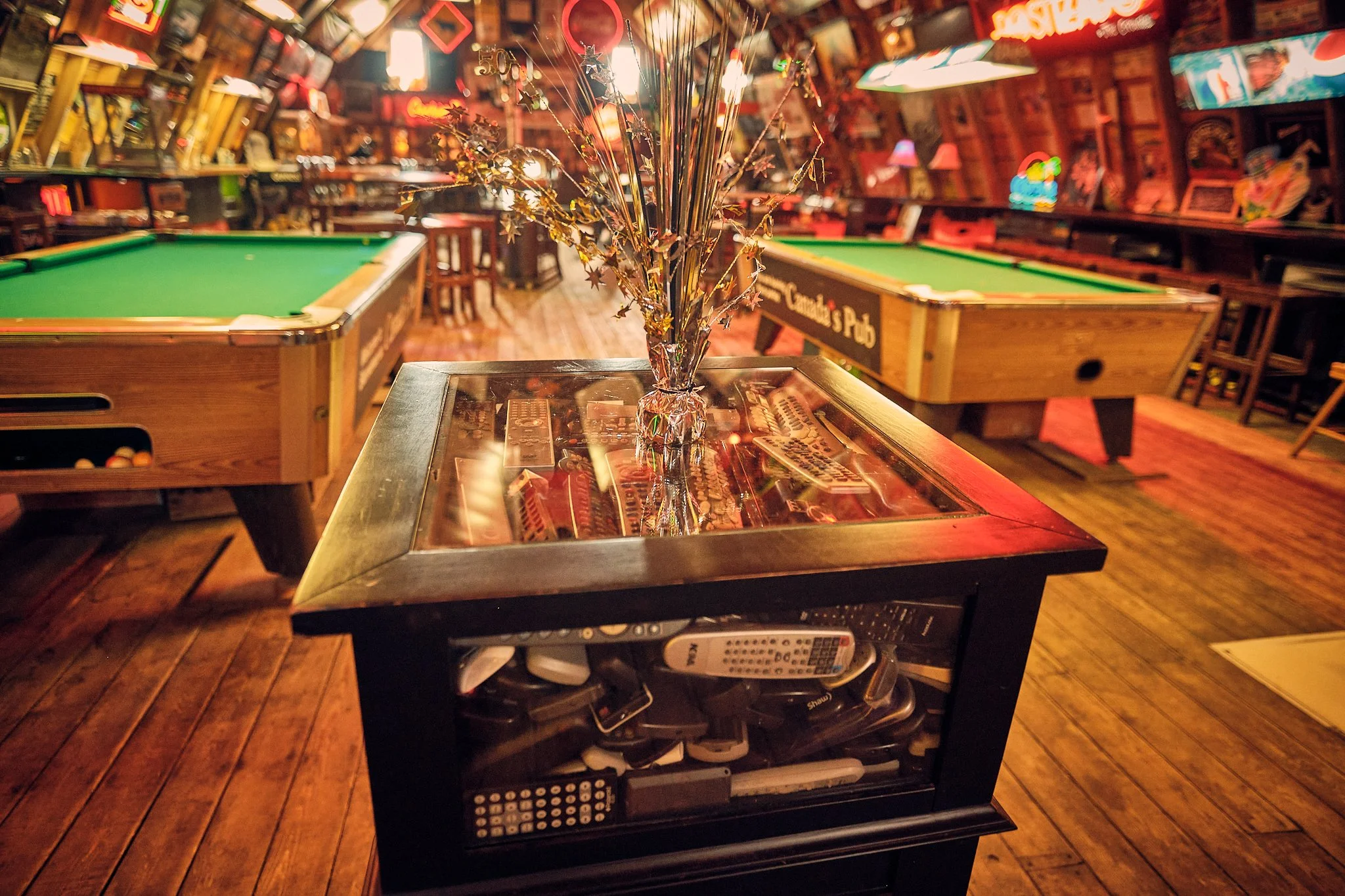 Decorative star-shaped metallic tinsel in a glass vase on top of a jukebox, with pool tables and neon lights in a cozy bar or game room setting.
