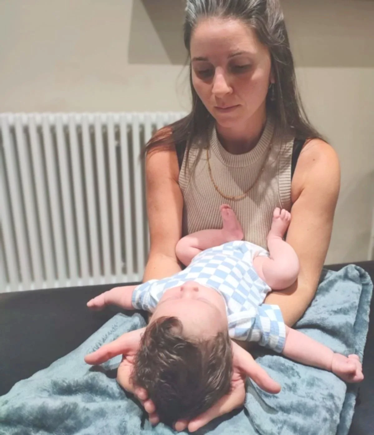 A woman holding an infant on a blanket, with a radiator in the background.