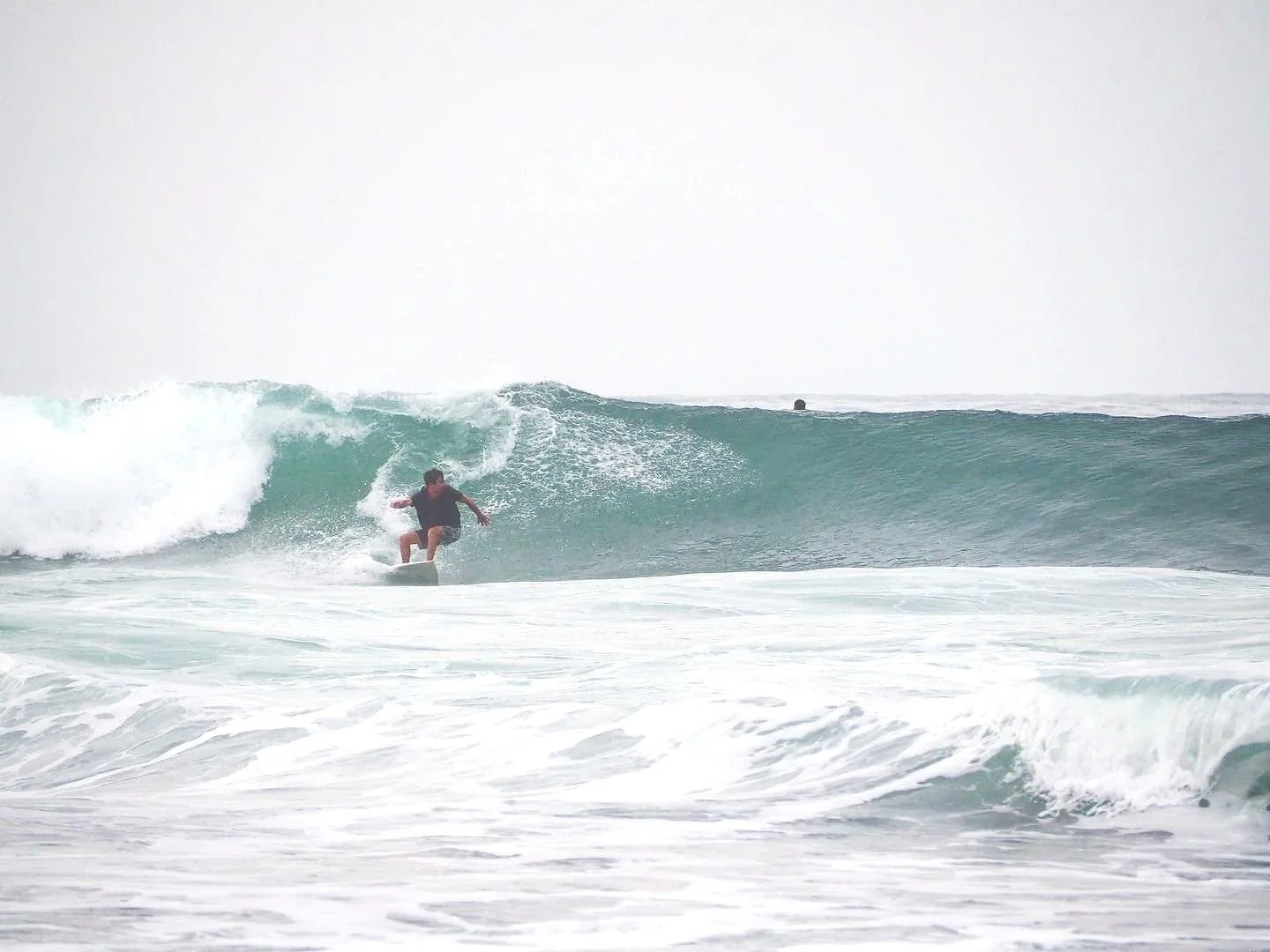A person surfing on a wave at the beach, with overcast sky in the background.