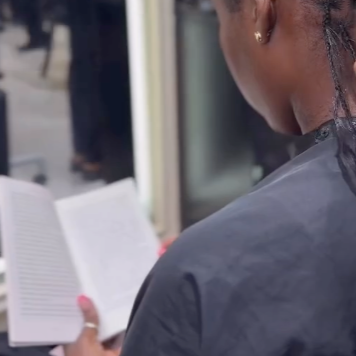 Person reading 'all about love' by bell hooks while having her hair braided in a salon in Ikeja, Lagos, Nigeria.