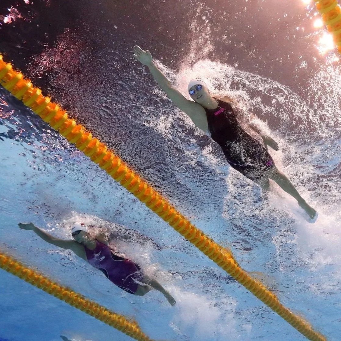 Swimmers competing in a swimming race in a pool, with lane markers visible and water splashing around them.