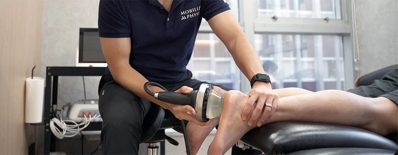 Physical therapist using ultrasound therapy device on a patient's ankle in a clinic.