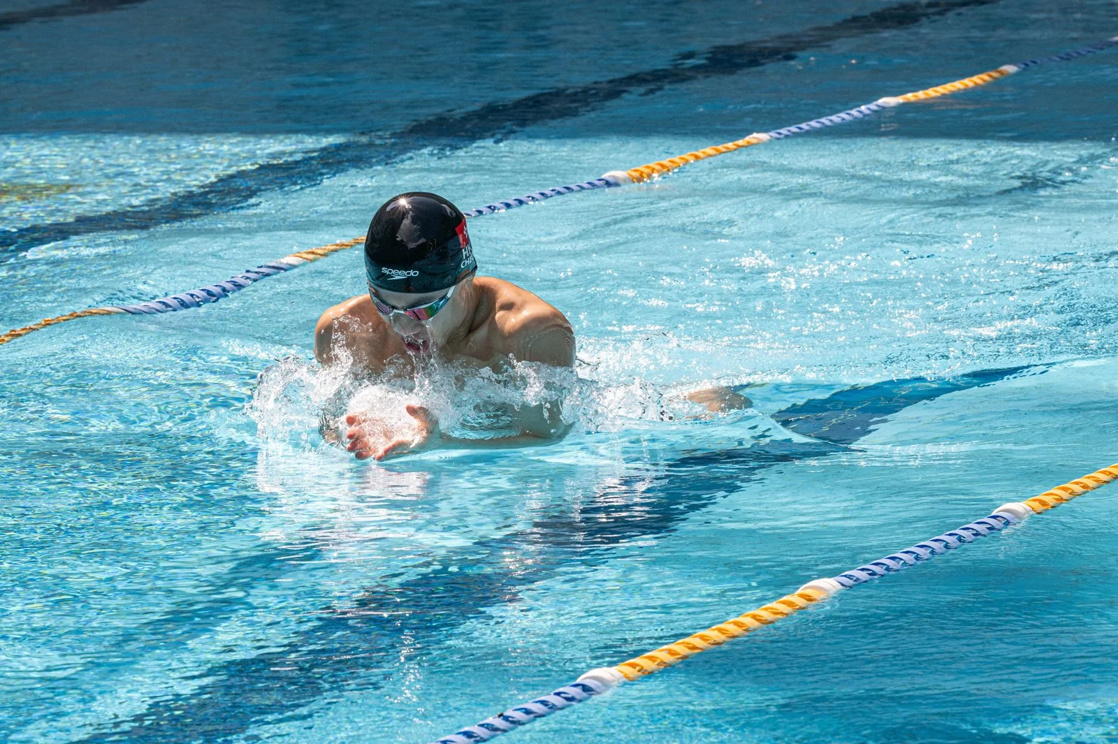 Swimmer performing a breaststroke in a swimming pool, wearing a black swim cap and goggles, surrounded by lane markers.