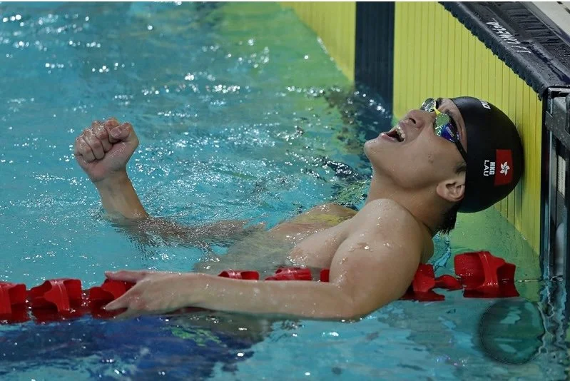 Swimmer celebrating after winning a race in a swimming pool, wearing a swim cap and goggles, with a joyful expression.