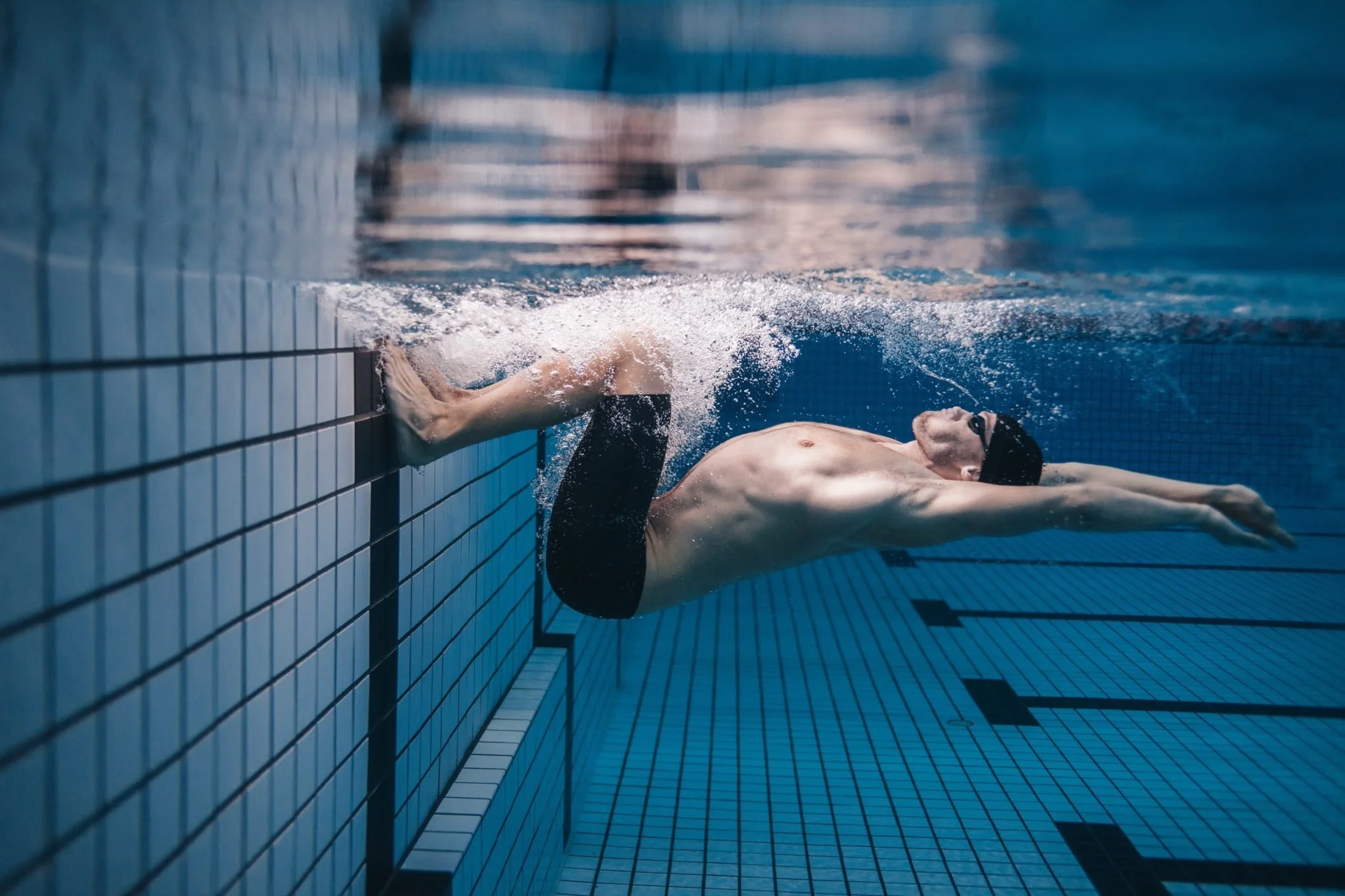 Swimmer underwater at the wall of a swimming pool, touching the tiles with his hand.