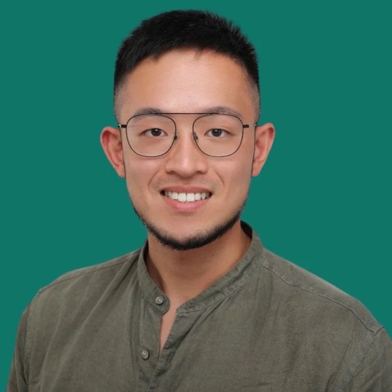 A young man with short black hair, glasses, and facial hair, smiling and wearing a button-up shirt against a solid teal background.
