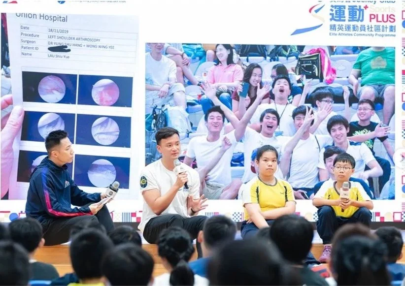 Panel discussion at a community event with a large screen in the background displaying medical images and a group of young participants.