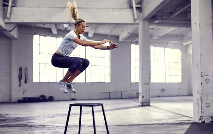 A woman jumps onto a stool in a spacious industrial-style gym