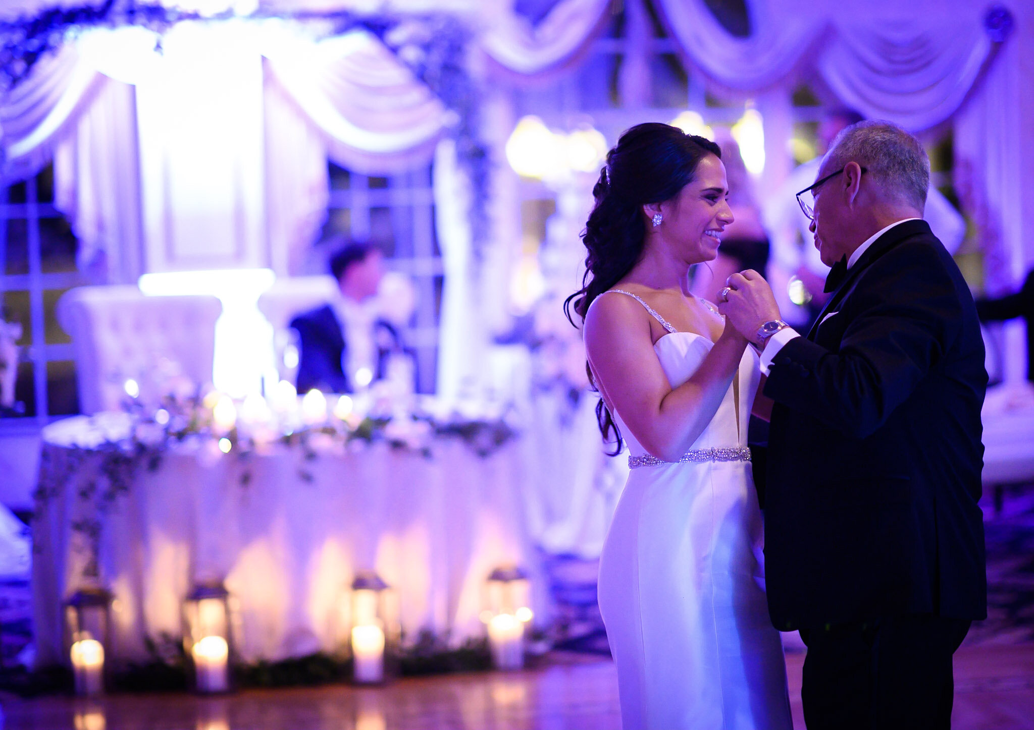 A bride and groom dance closely at their wedding reception in a decorated venue with purple lighting.