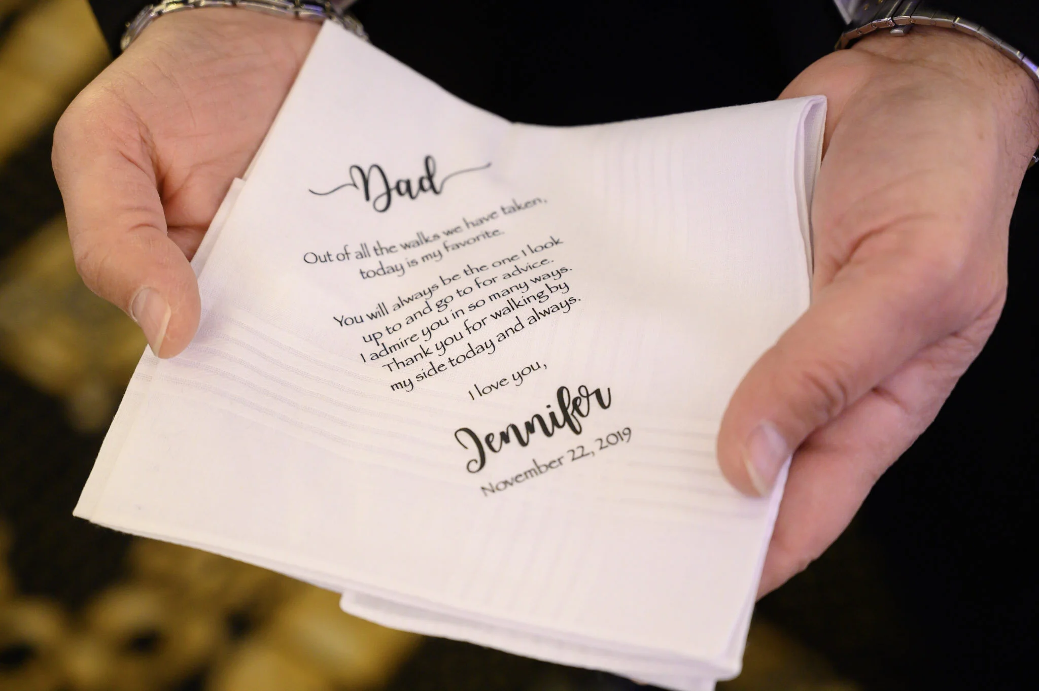 Close-up of hands holding a folded white napkin with a heartfelt handwritten note from a daughter to her dad, expressing love and appreciation.