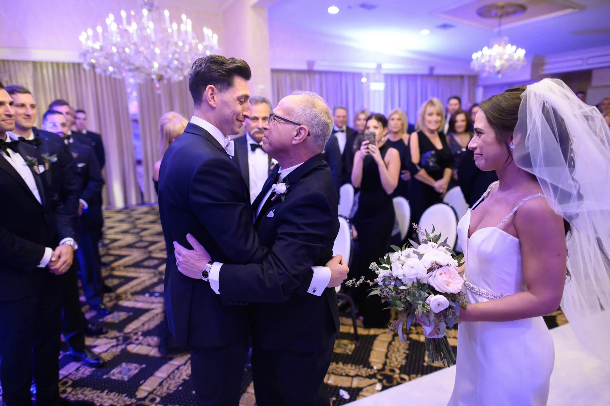 A wedding ceremony with a groom and bride exchanging vows, surrounded by guests in an elegant ballroom.