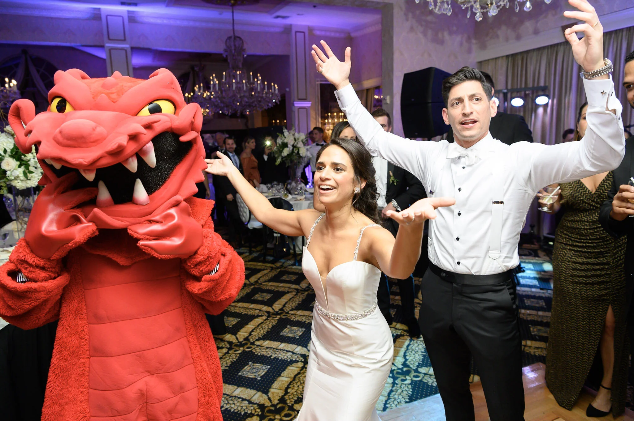 People dancing at a celebration with a person in a pink monster costume.