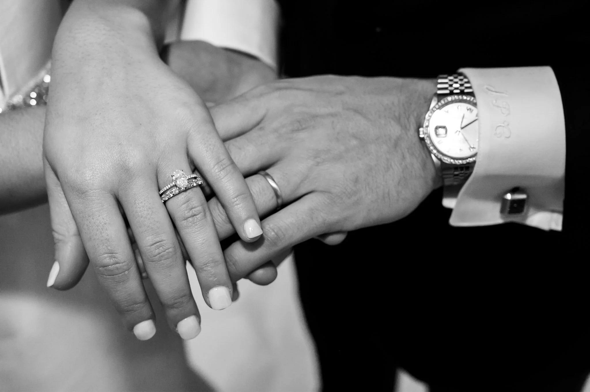 Black and white photo of a man and woman holding hands, showing engagement and wedding rings.