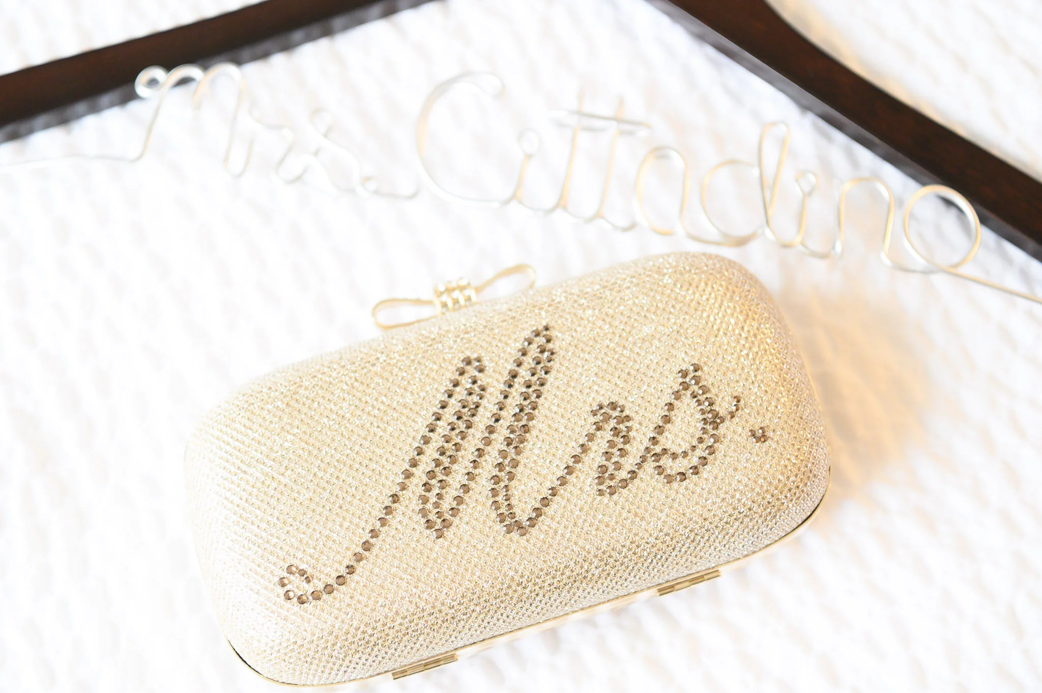 A beige clutch purse decorated with rhinestones, with the name 'Chanel' spelled out in rhinestones on the front, resting on a white textured surface.