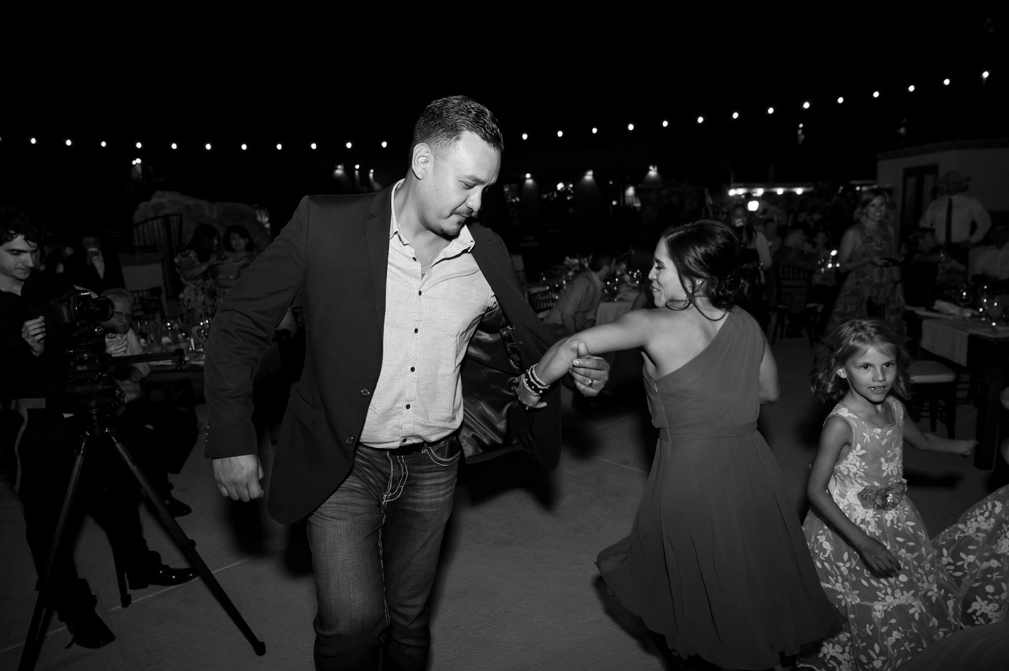 A man and woman dance together at an outdoor evening event, surrounded by other guests and photographers.