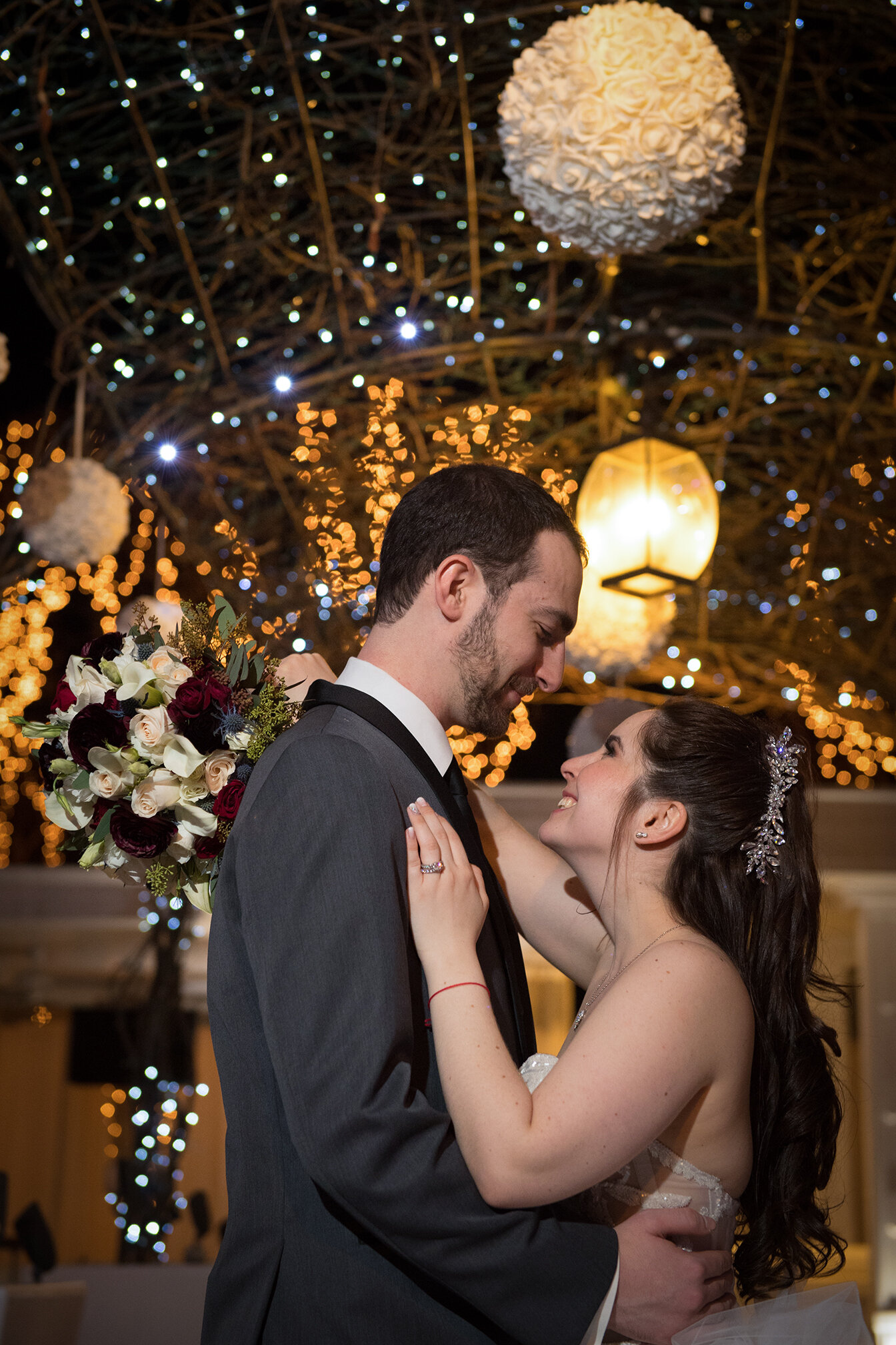 A bride and groom dancing at their wedding reception with decorative string lights and floral arrangements in the background.