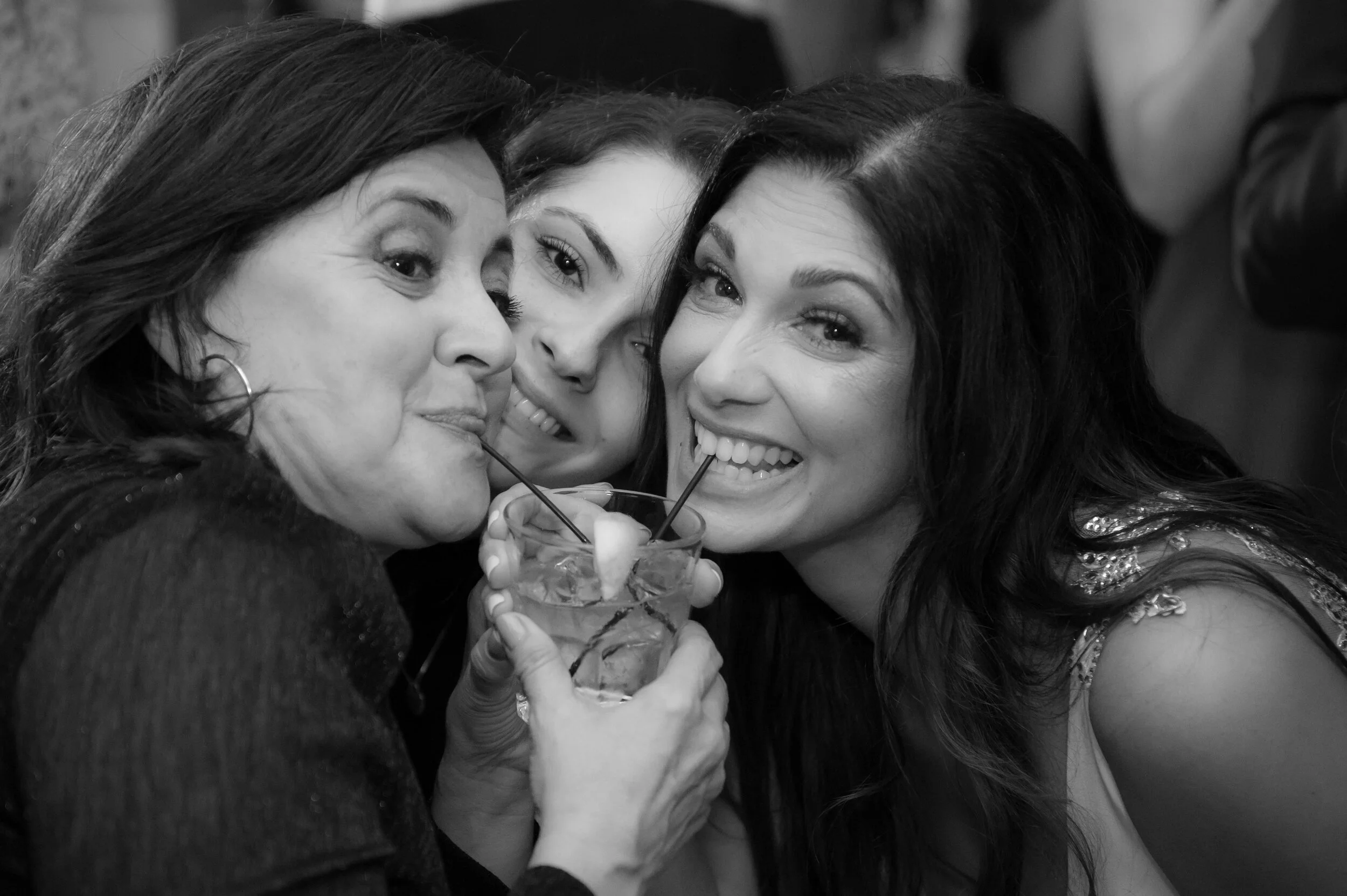 Group of three women sharing a drink together, smiling, close-up shot, black and white