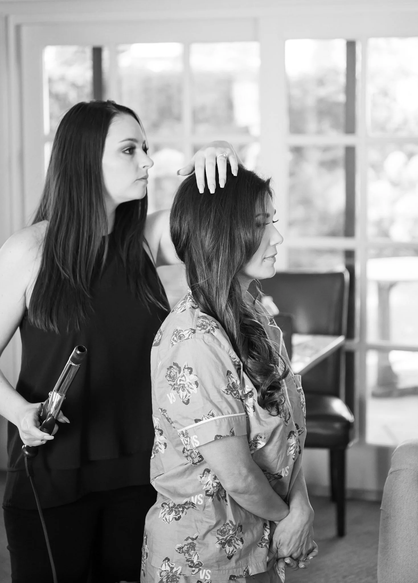 A woman with long dark hair getting her hair done by a hairstylist in a salon.