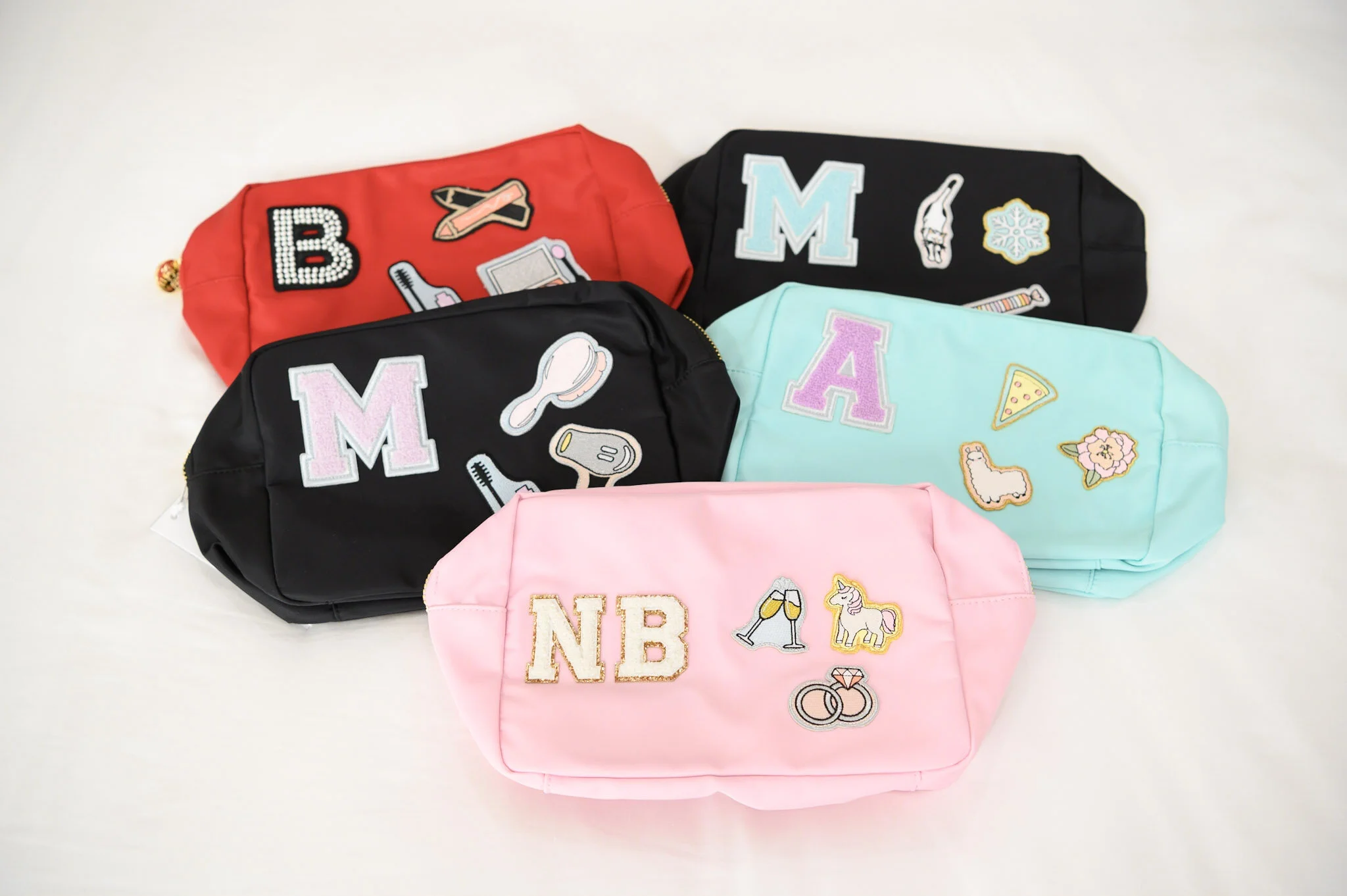 Four colorful pouches with embroidered patches and initials, arranged on a white background.