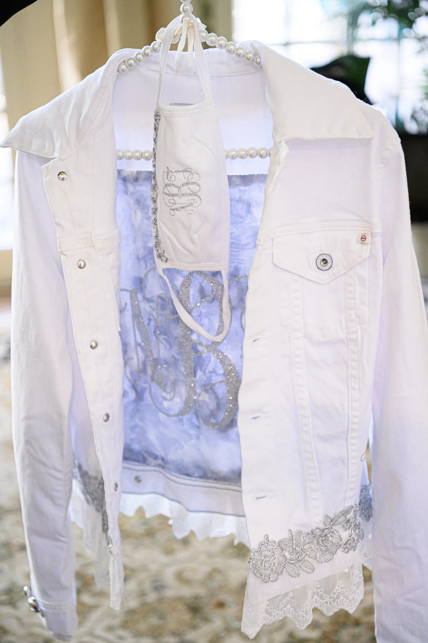 White clothing, including a jacket and a dress, hanging on a beaded hanger with a small decorative purse. The jacket has floral embroidery at the bottom.