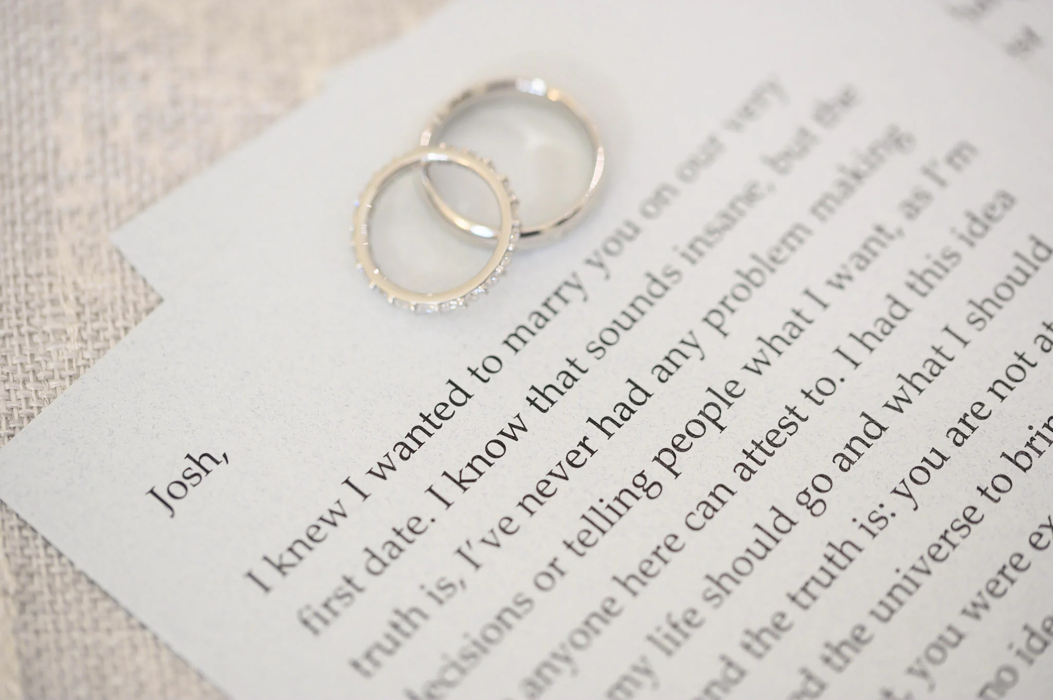 Close-up of two wedding rings placed on a white piece of paper with printed text, on a textured surface.