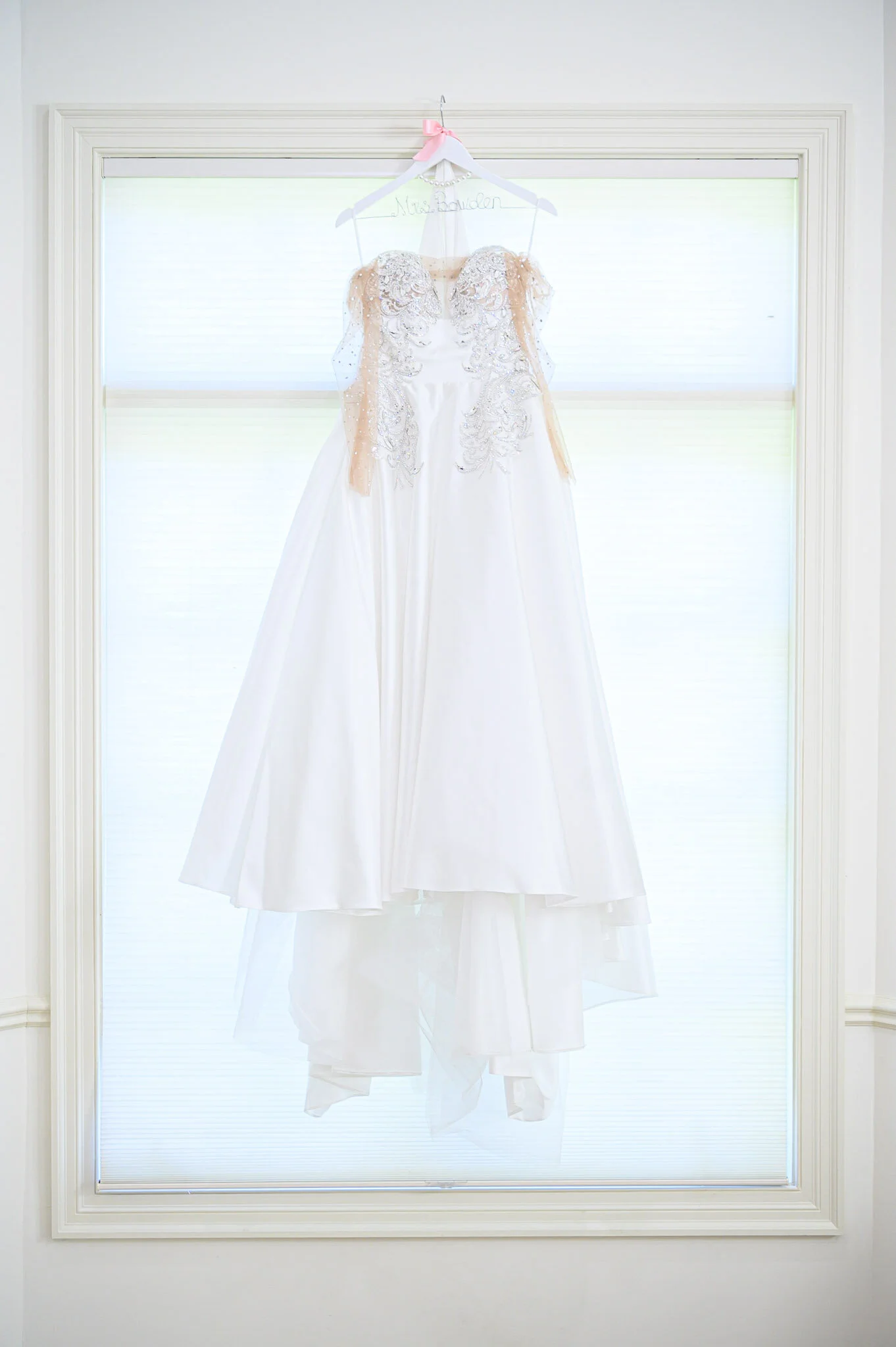 Wedding dress hanging on a colorful window with white blinds.