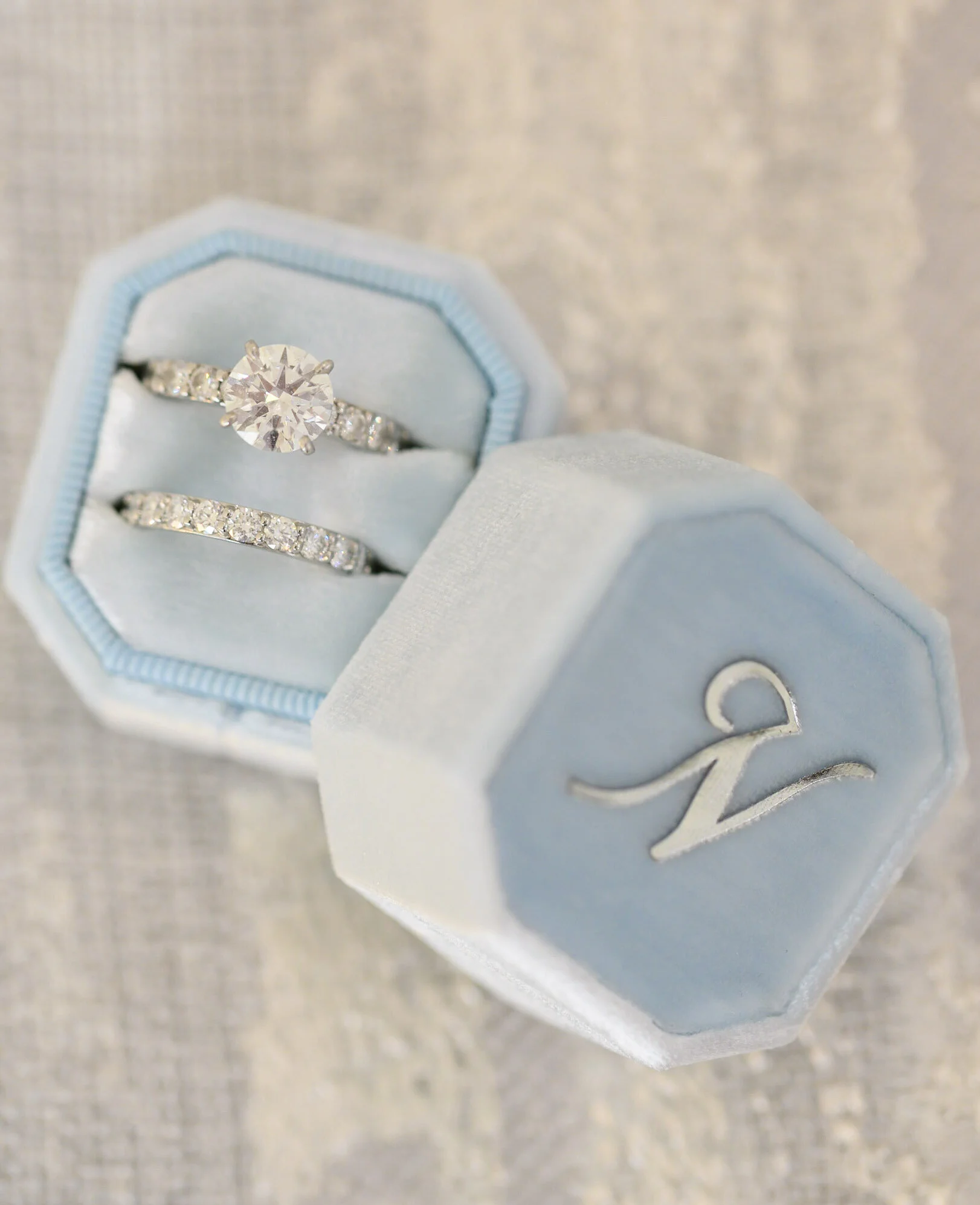 Close-up of a diamond engagement ring with a large center stone and smaller stones on the band, inside a light blue jewelry box.