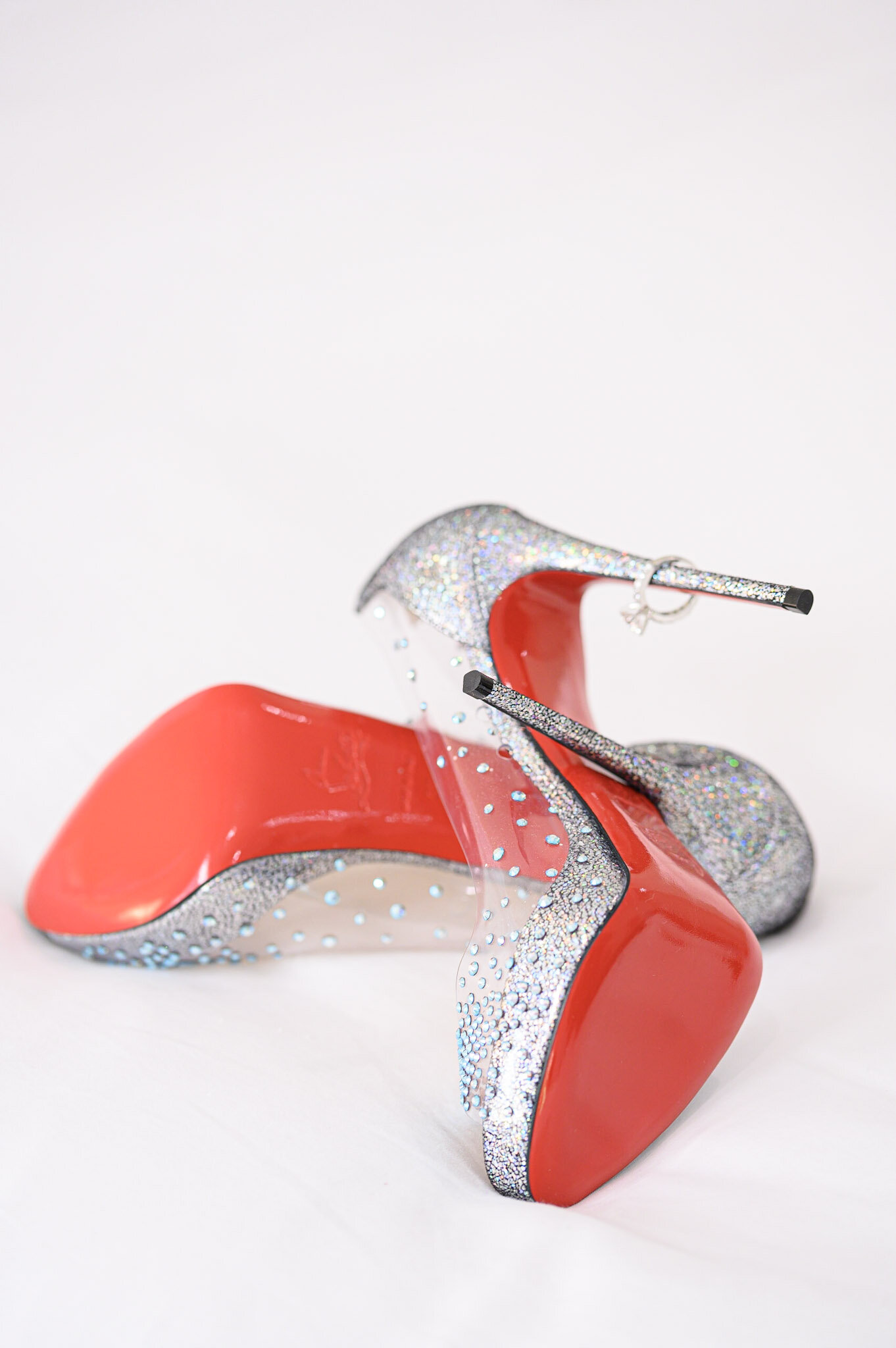 A colorful high-heeled shoe with a red sole, glittery silver accents, and a clear heel, against a plain white background.