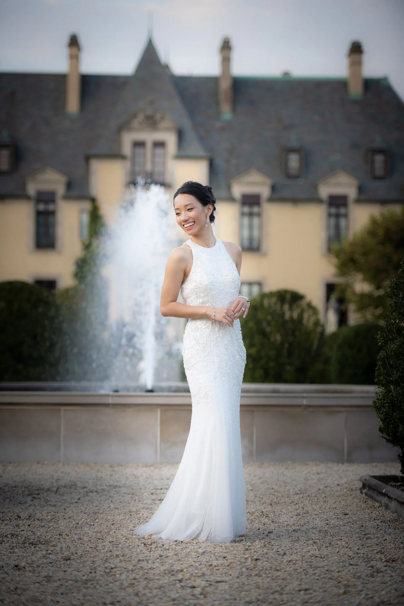 A bride in a white wedding dress standing outdoors in front of a fountain and a large historic building.
