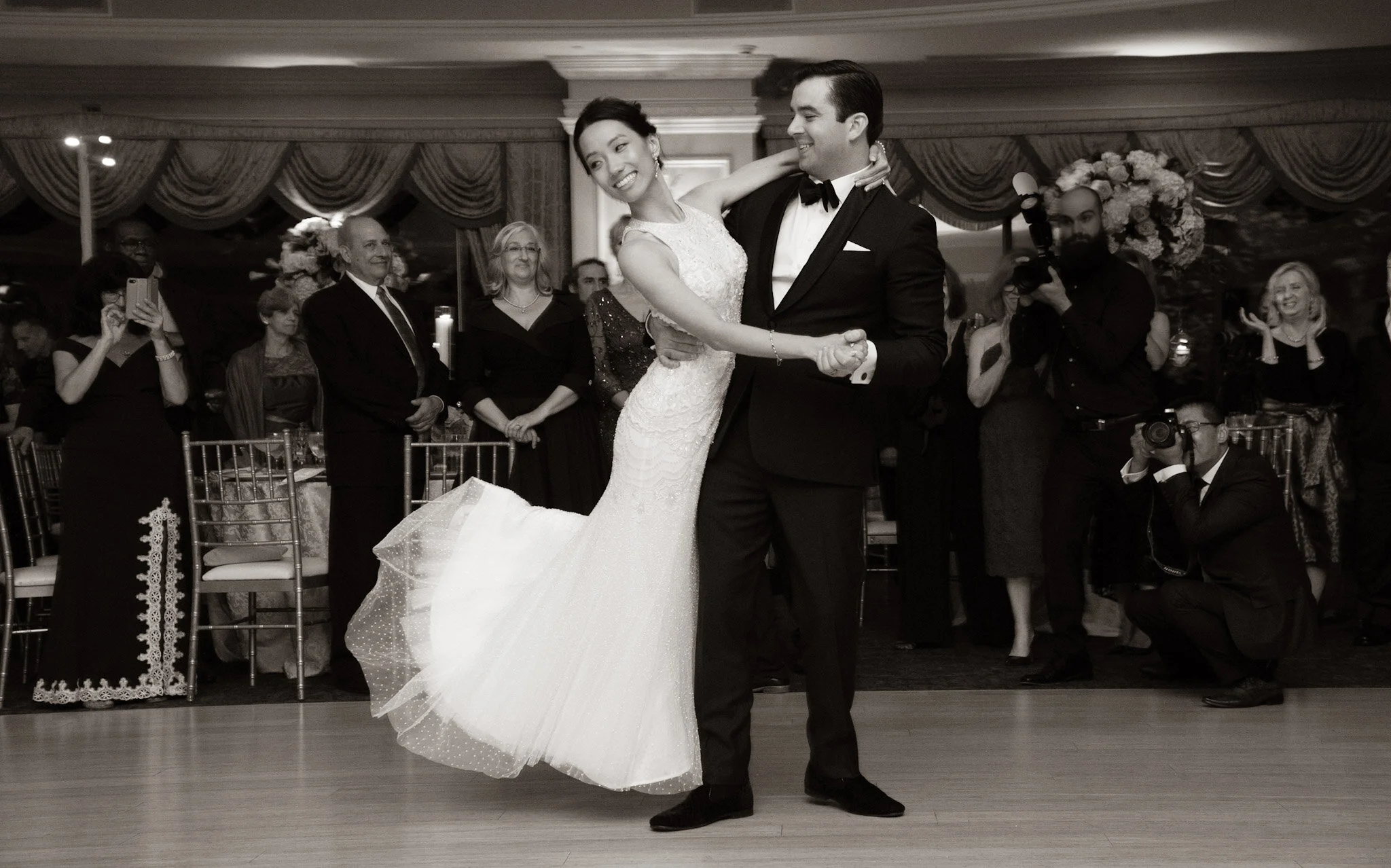 A bride and groom dancing at a wedding reception surrounded by well-dressed guests.
